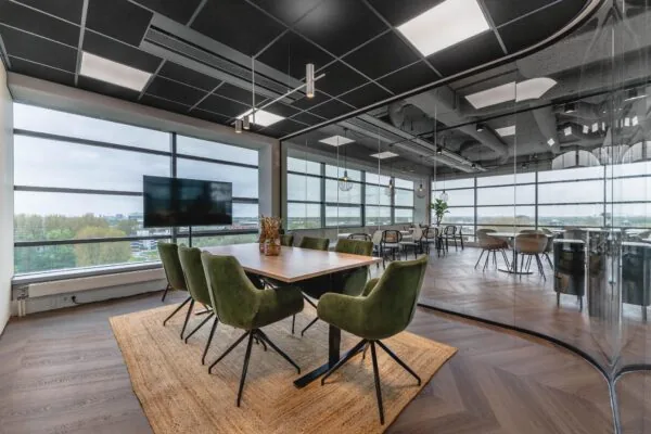 Moderne vergaderruimte aan de Joop Geesinkweg met glazen wanden, groenfluwelen stoelen en uitzicht op de stad.