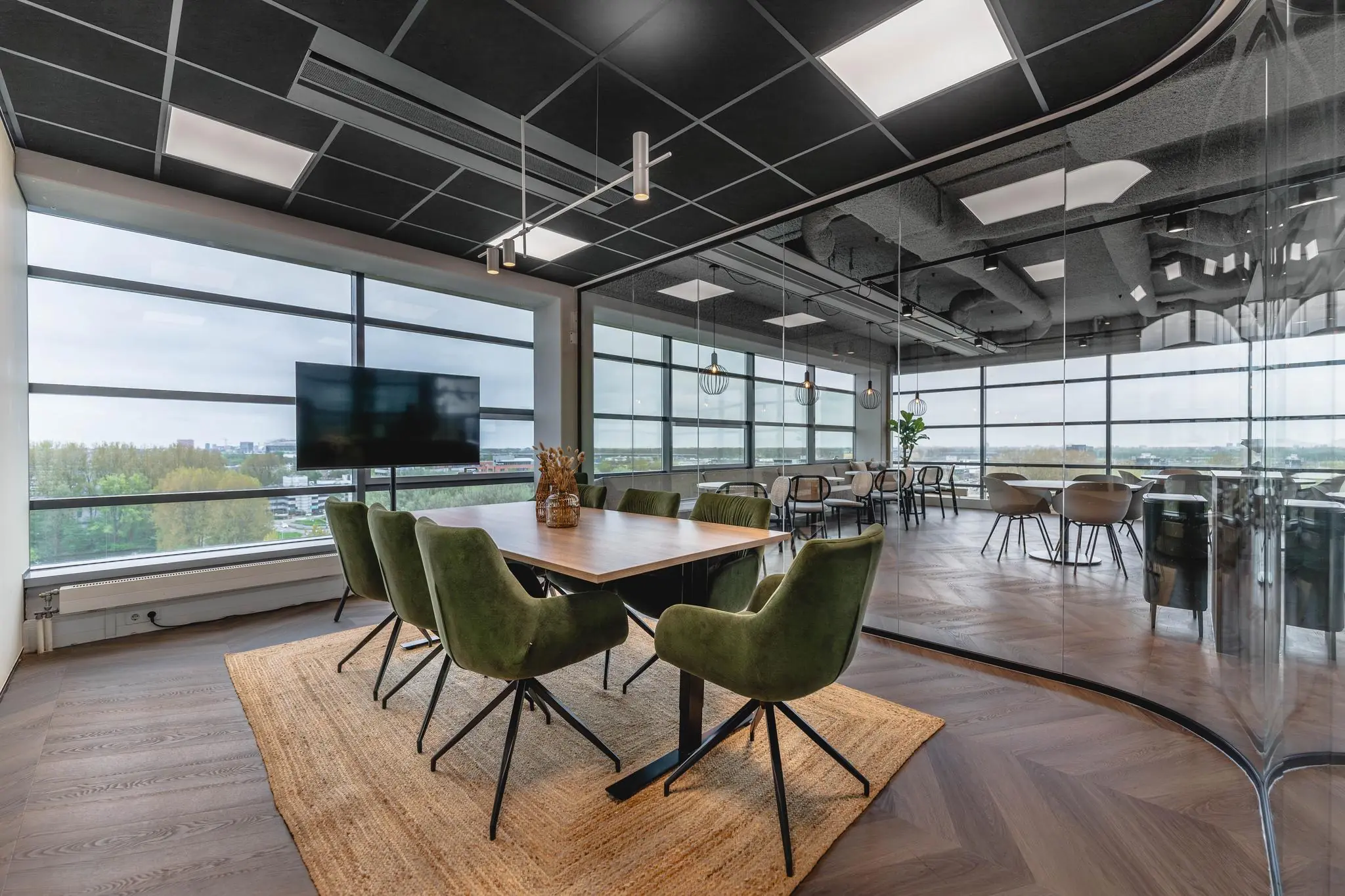 Moderne vergaderruimte aan de Joop Geesinkweg met glazen wanden, groenfluwelen stoelen en uitzicht op de stad.