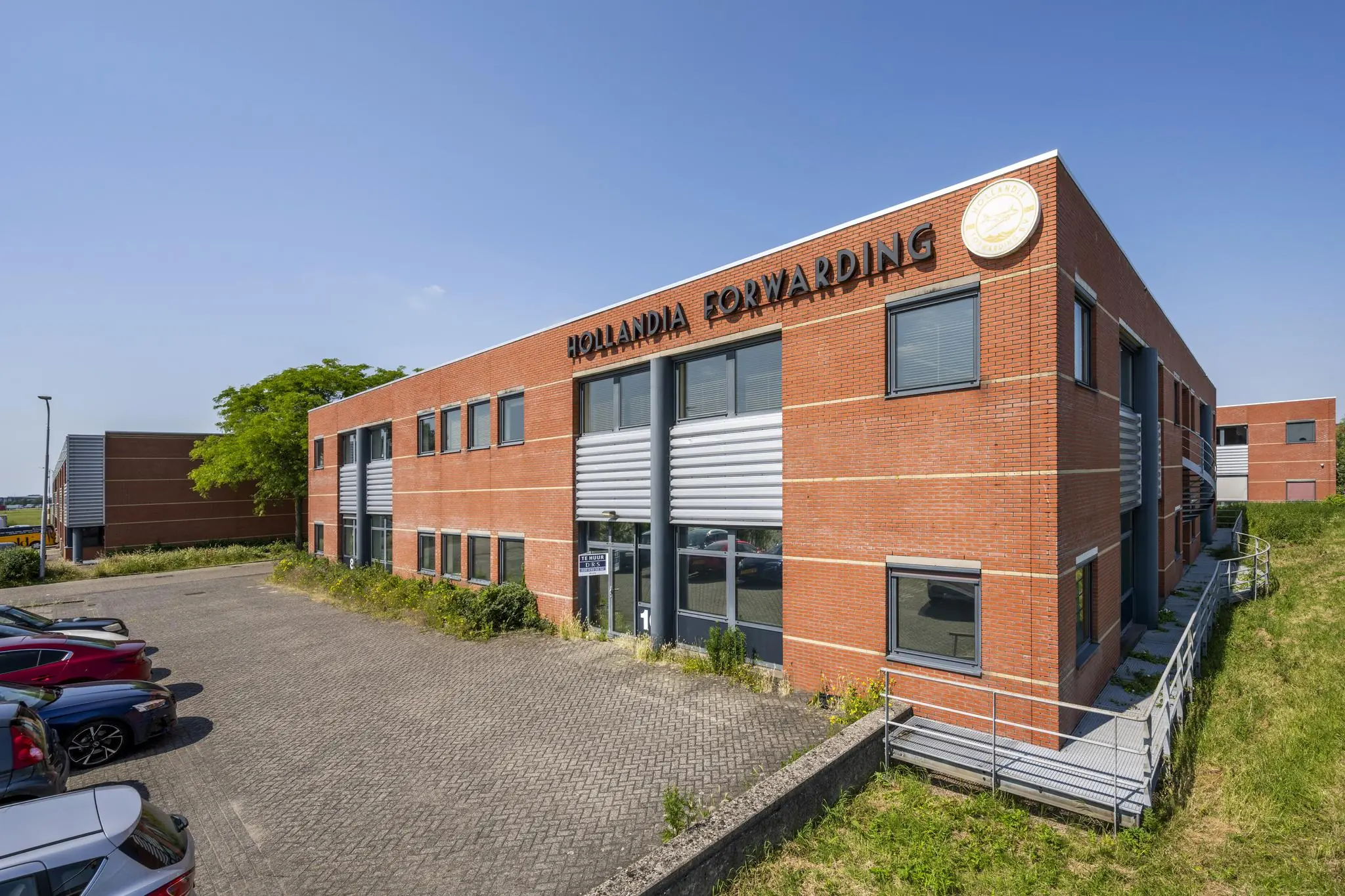 Modern bedrijfspand van Hollandia Forwarding aan de Breguetlaan, met rode bakstenen gevel en parkeerterrein.