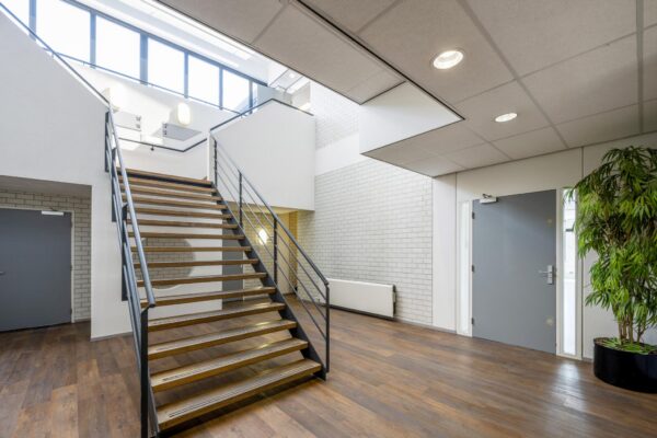 Moderne, lichte entreehal met houten trap, grijze deuren en een grote plant aan de Breguetlaan.