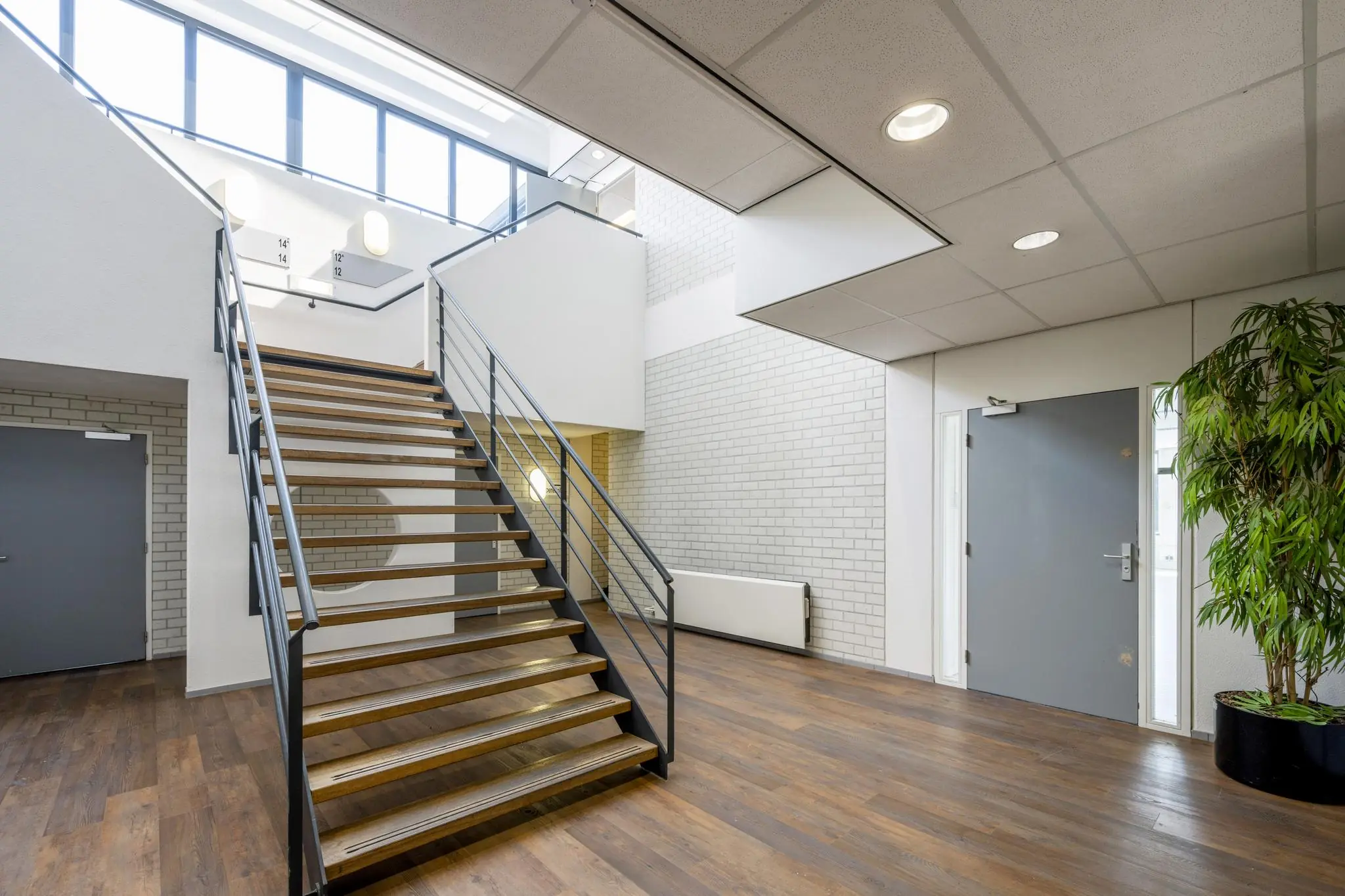 Moderne, lichte entreehal met houten trap, grijze deuren en een grote plant aan de Breguetlaan.