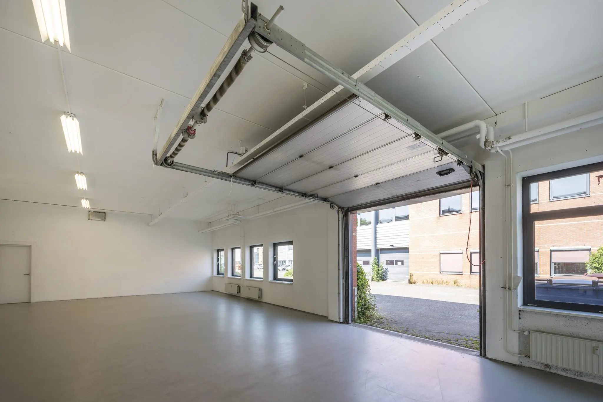 Lichte en lege bedrijfsruimte aan de Breguetlaan met open overheaddeur en zicht op het buitenterrein.