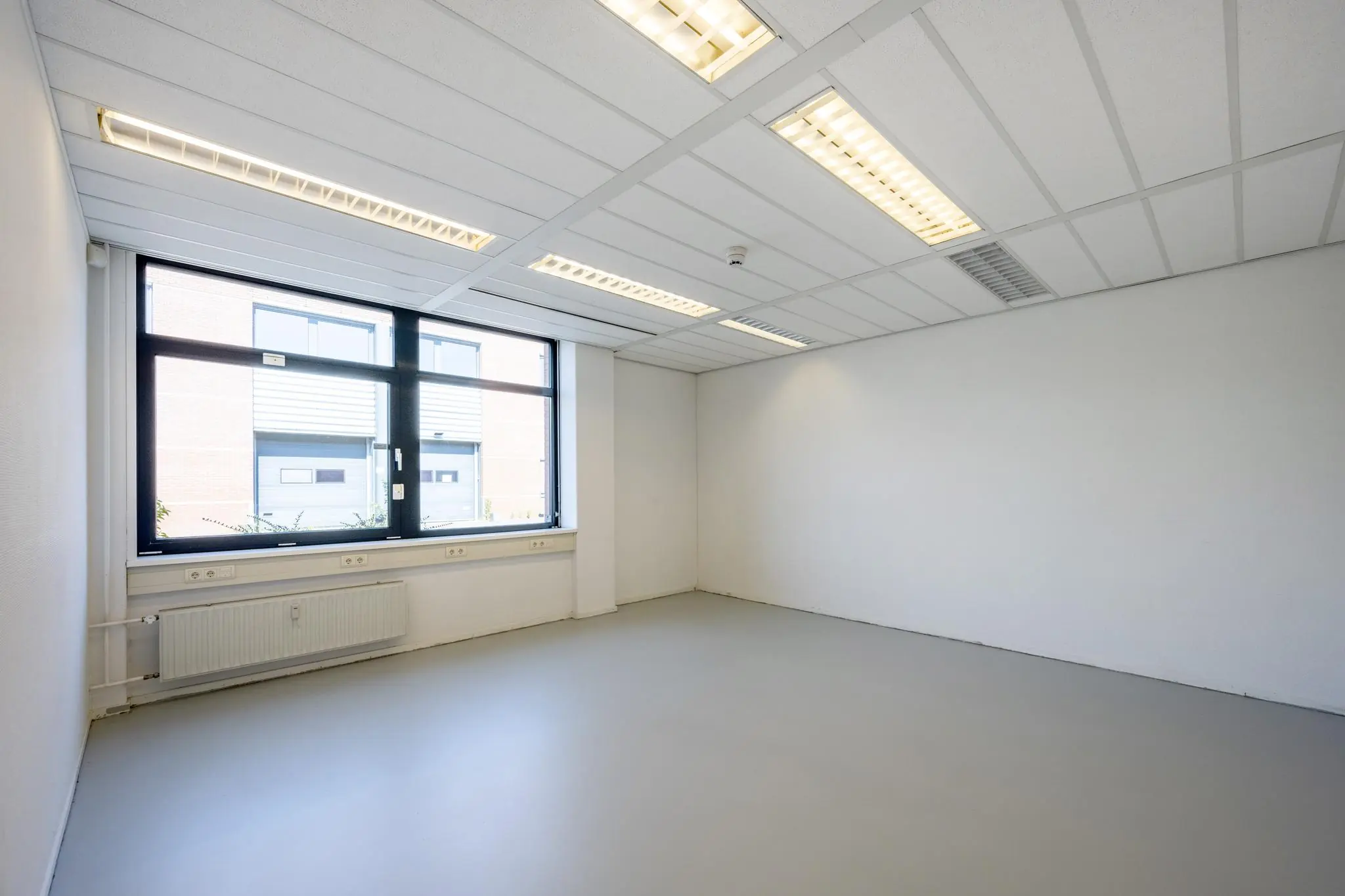 Leeg, licht kantoor met grote ramen en systeemplafond aan de Breguetlaan.