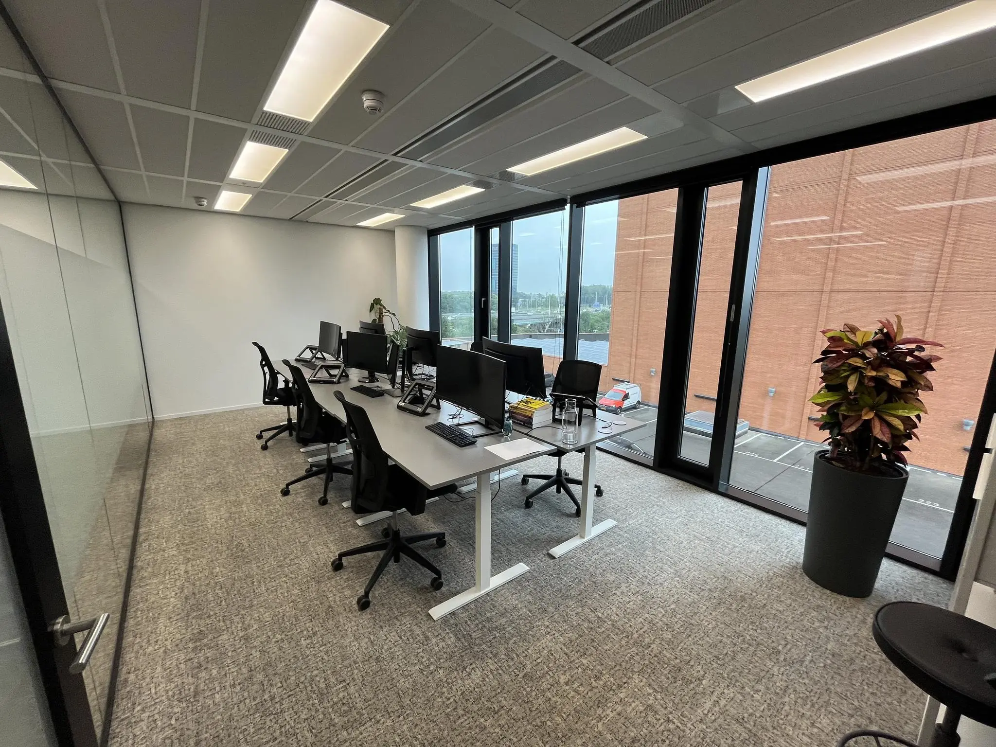 Moderne kantoorkamer aan de Winthontlaan met werkplekken, computers en grote ramen met uitzicht op een parkeergarage.