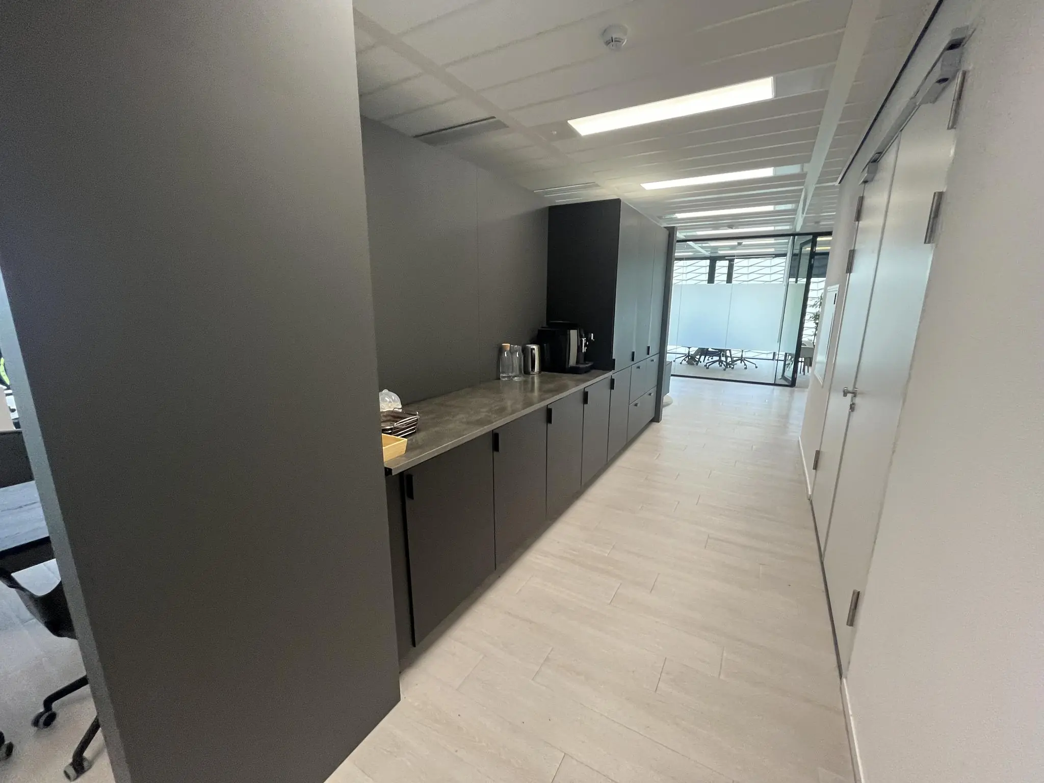 Moderne kantoorpantry aan de Winthontlaan met koffiezetapparaat, kasten en glazen deuren naar vergaderruimte.