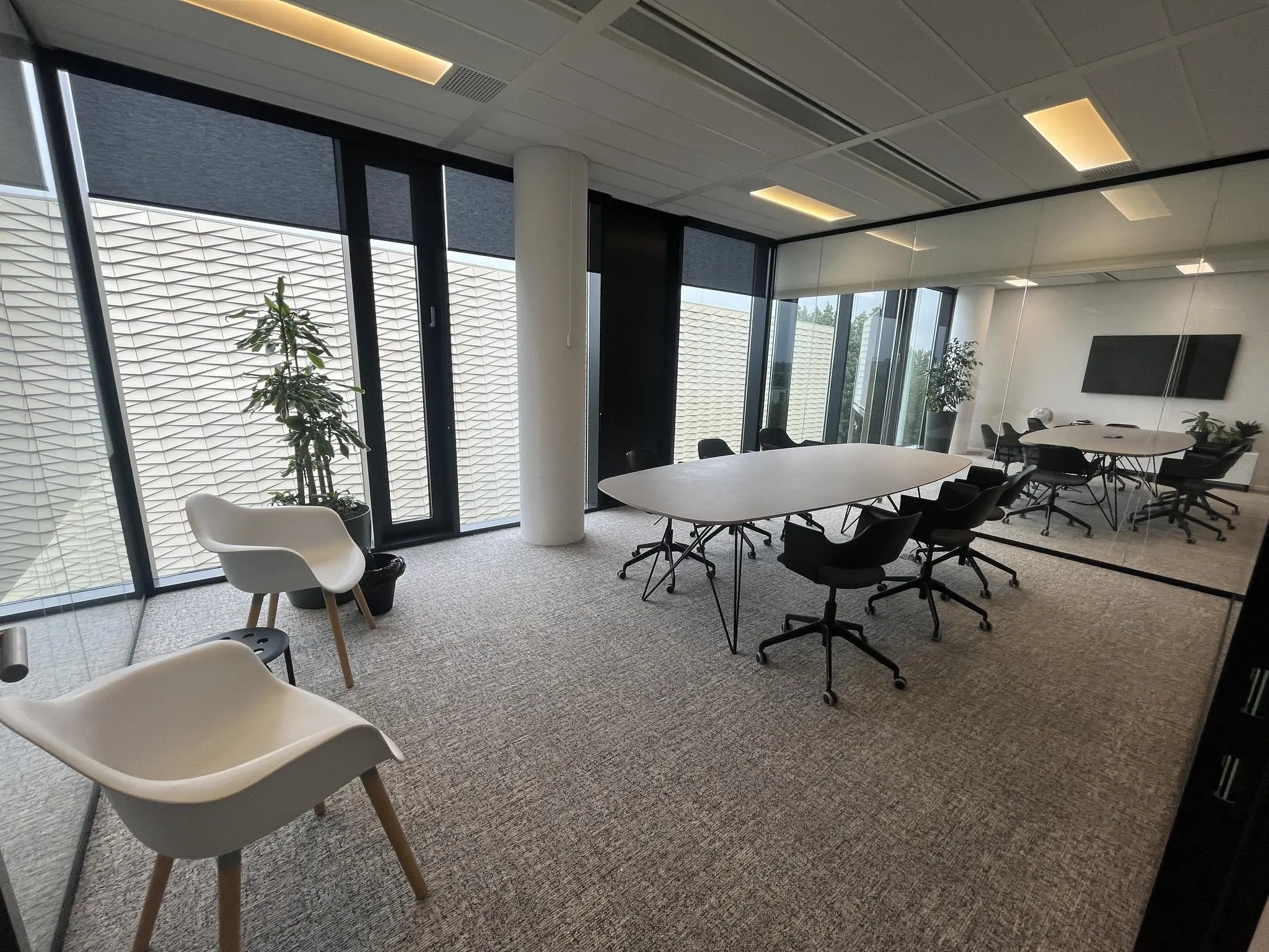 Moderne vergaderruimte aan de Winthontlaan met glazen wanden, zwarte stoelen, ovale tafel en grote ramen.
