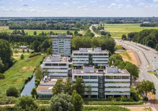 Luchtfoto van kantoorgebouwen aan de Burgemeester Stramanweg in een groen landschap met naastgelegen snelweg.