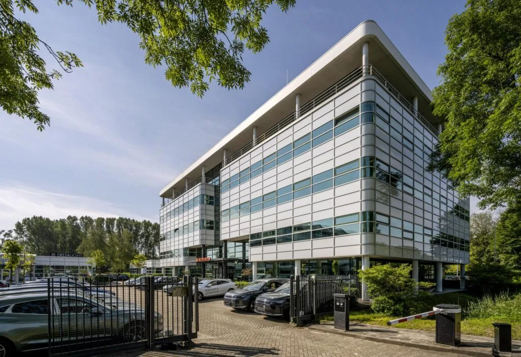 Modern kantoorgebouw aan de Burgemeester Stramanweg met glazen gevel en parkeergelegenheid op de voorgrond.