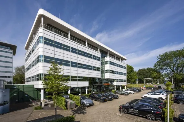 Modern kantoorgebouw aan de Burgemeester Stramanweg met parkeerterrein vol geparkeerde auto's.