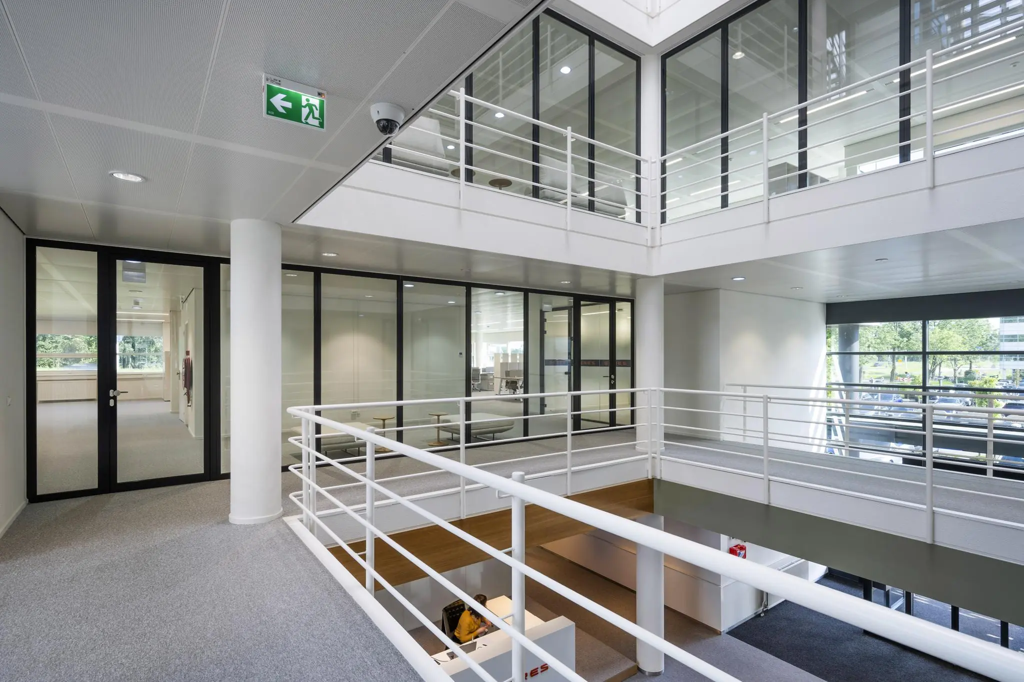 Modern interieur van een kantoorpand aan de Burgemeester Stramanweg met glazen wanden, witte balustrades en zicht op de receptie beneden.