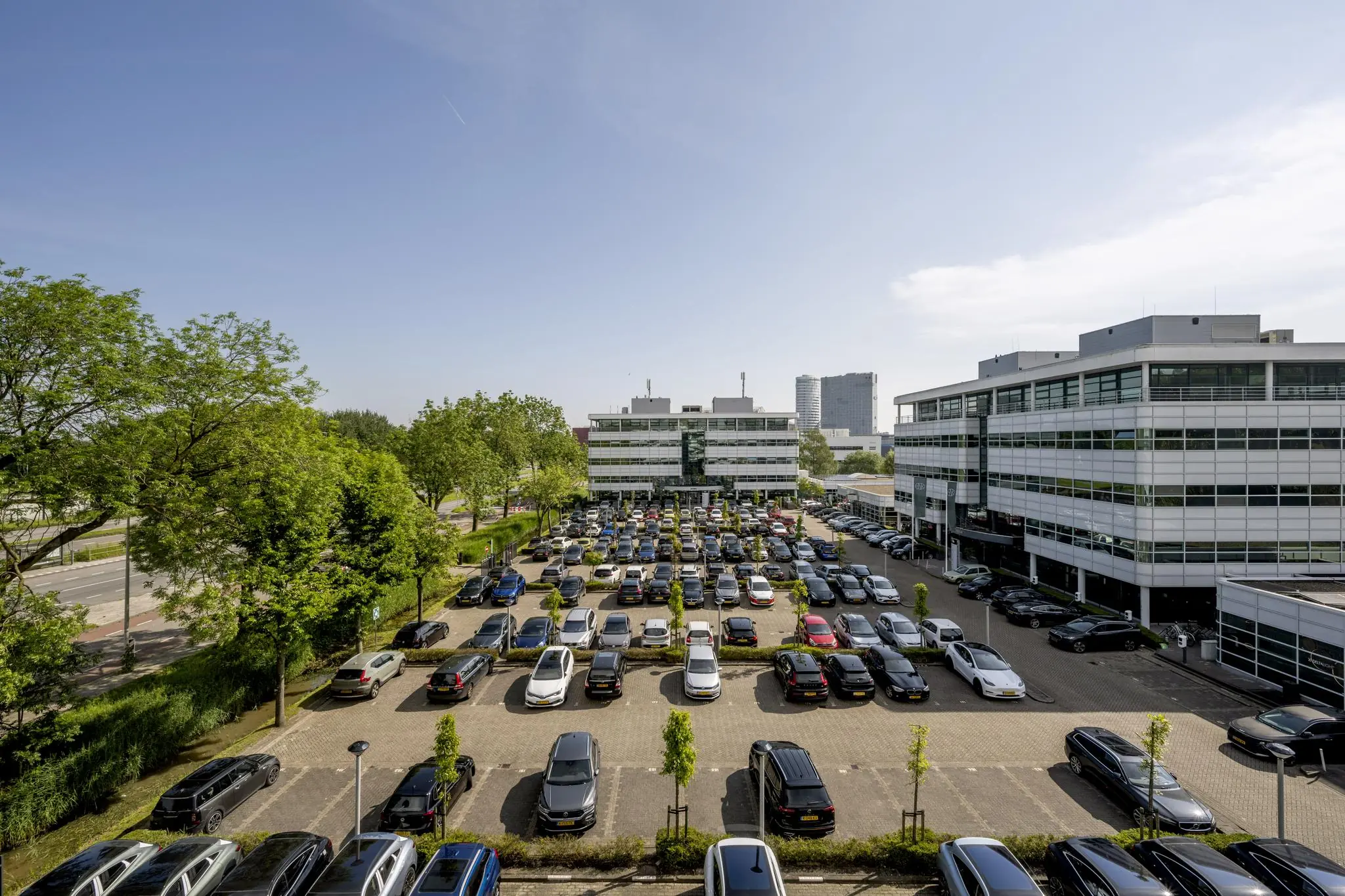 Groot parkeerterrein vol auto's tussen moderne kantoorgebouwen aan de Burgemeester Stramanweg in Amsterdam.