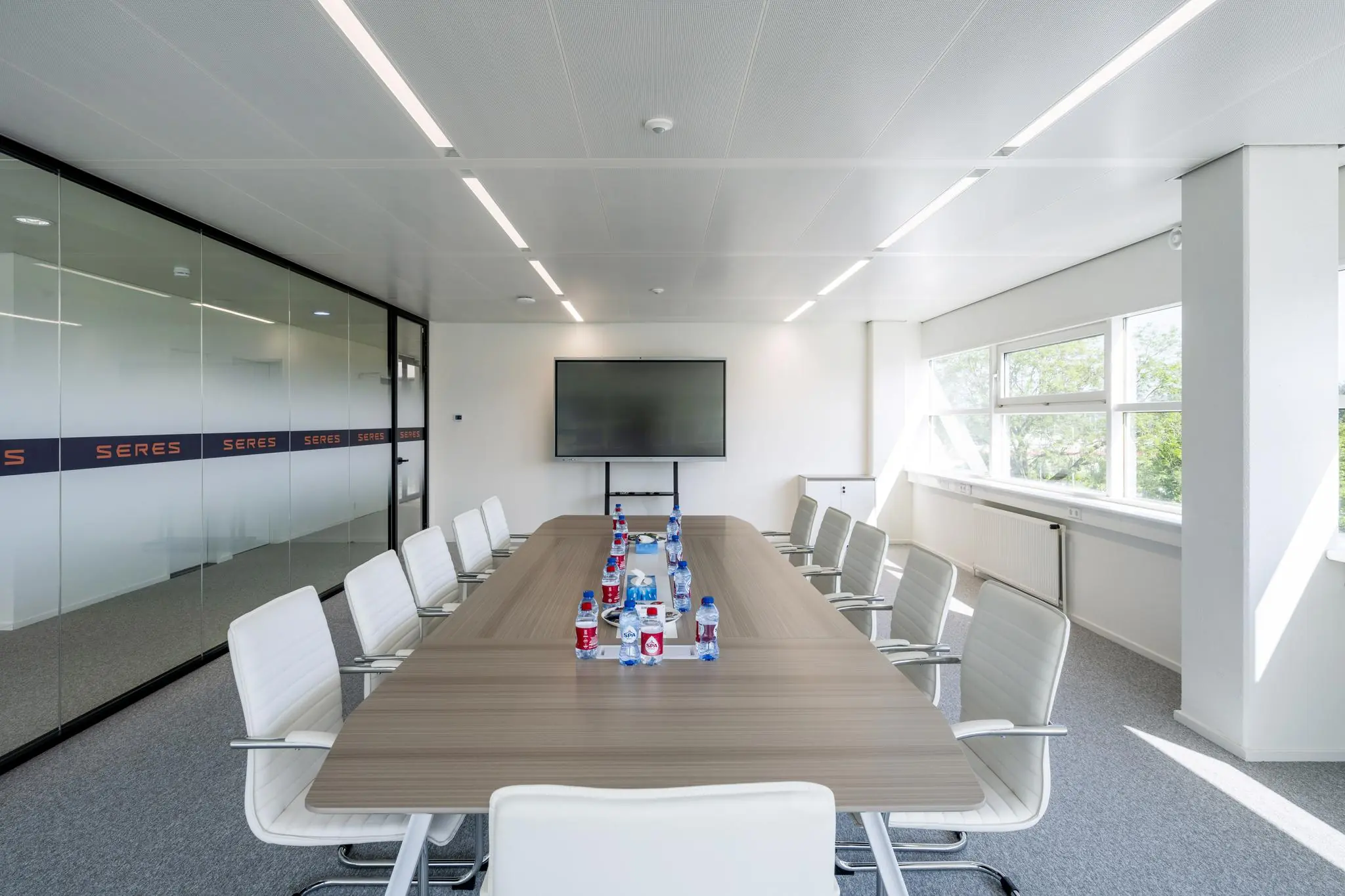Vergaderruimte aan de Burgemeester Stramanweg met een lange tafel, witte stoelen, een presentatiescherm en drinkwaterflesjes.