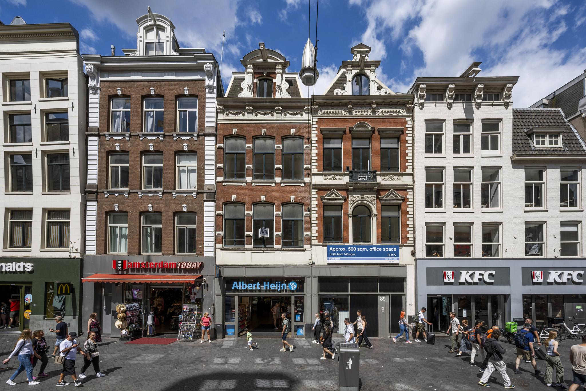 Winkelpanden en historische gebouwen aan het Damrak in Amsterdam met onder andere Albert Heijn, KFC en toeristenwinkel Amsterdam Today.