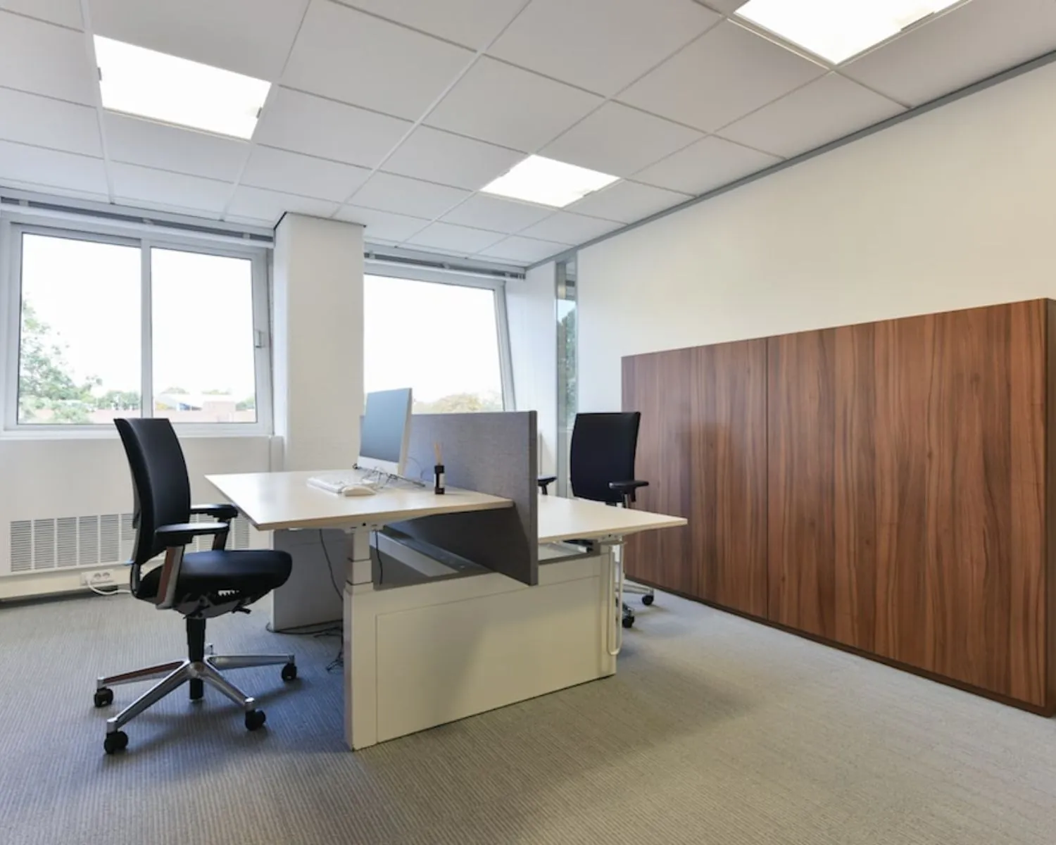 Moderne kantoorruimte met twee werkplekken, bureaustoelen en een groot houten opbergmeubel aan de Treubstraat 1 in Rijswijk.