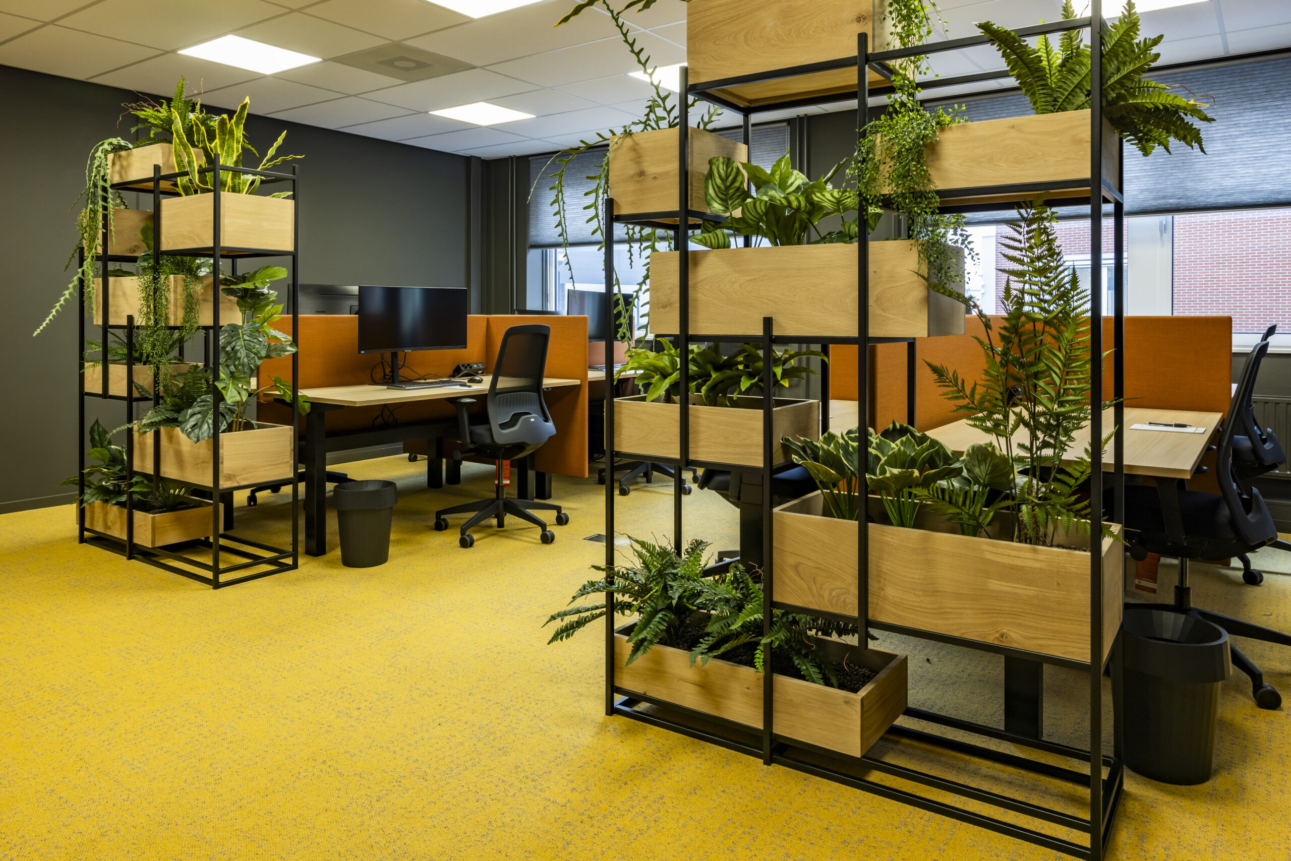 Een modern kantoor met veel planten in houten bakken en bureaustoelen op een gele vloer.
