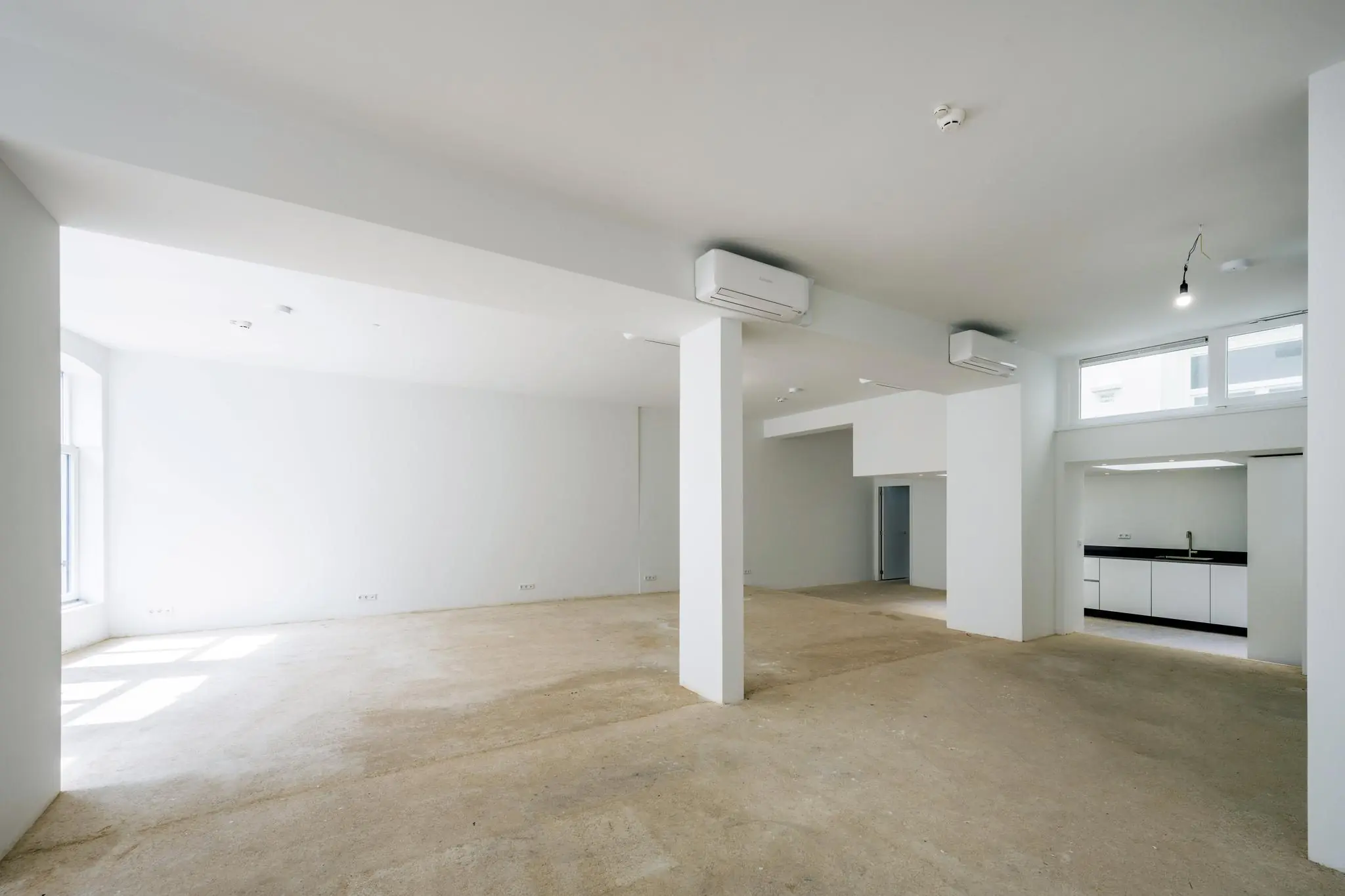 Ruime, lichte, casco commerciële ruimte aan het Damrak met wit afgewerkte wanden en een open keukenblok.