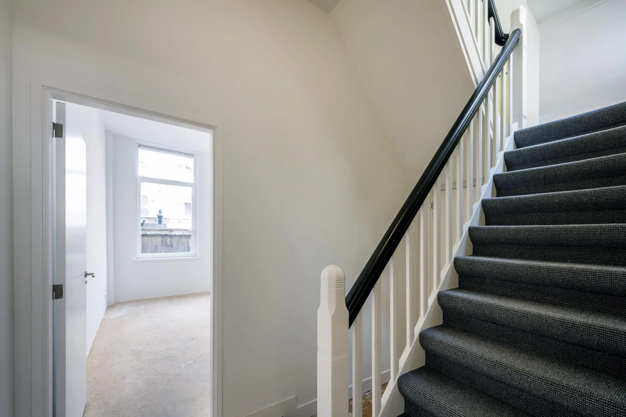 Trap met zwarte loper naast een lichte kamer met raam in een woning aan het Damrak.