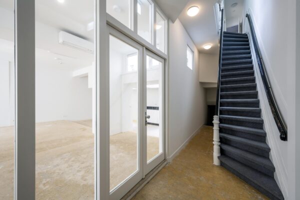 Ingang van een gerenoveerde woning aan het Damrak met zicht op een trap en glazen deuren naar een lege kamer.