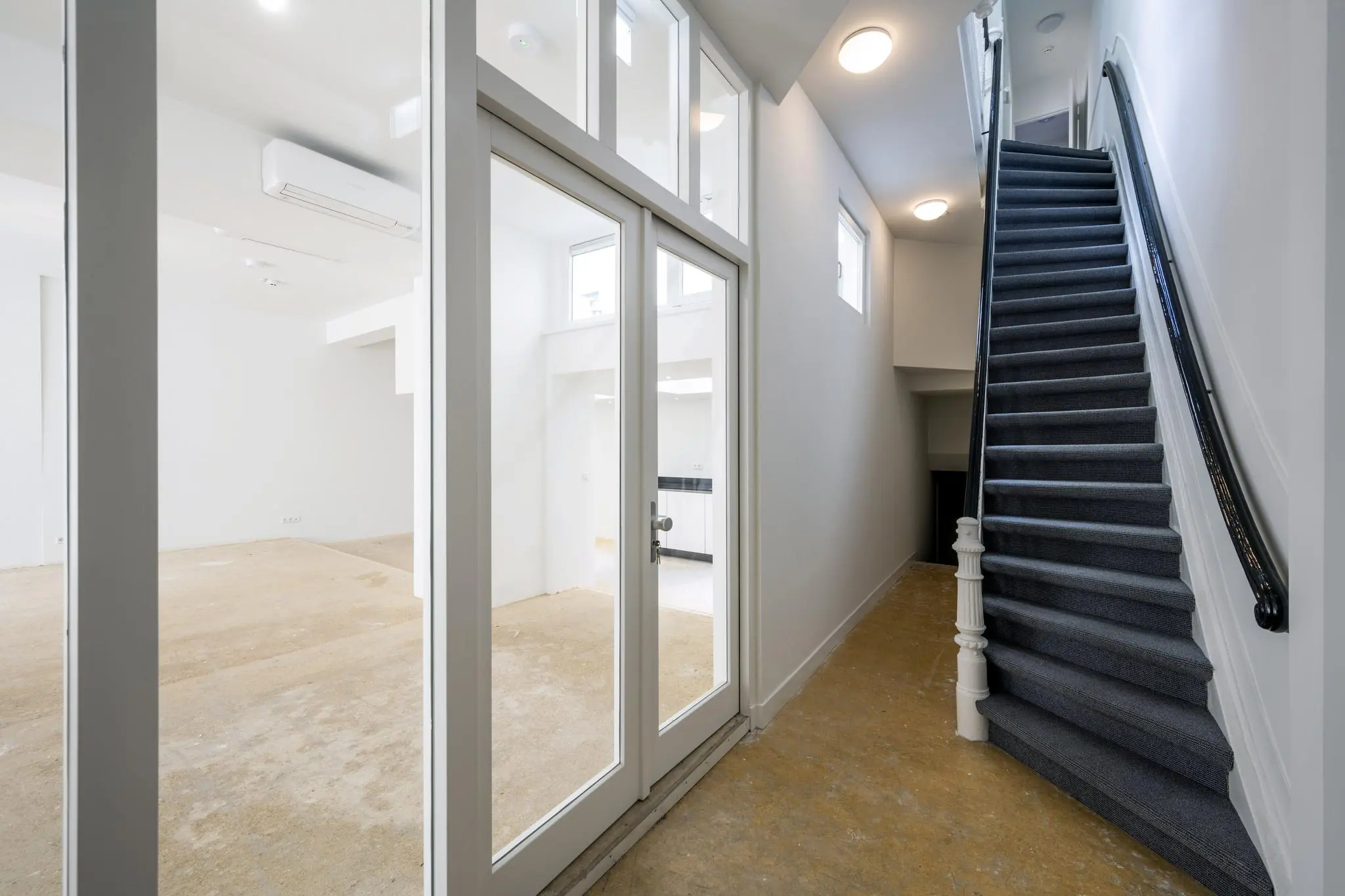 Ingang van een gerenoveerde woning aan het Damrak met zicht op een trap en glazen deuren naar een lege kamer.