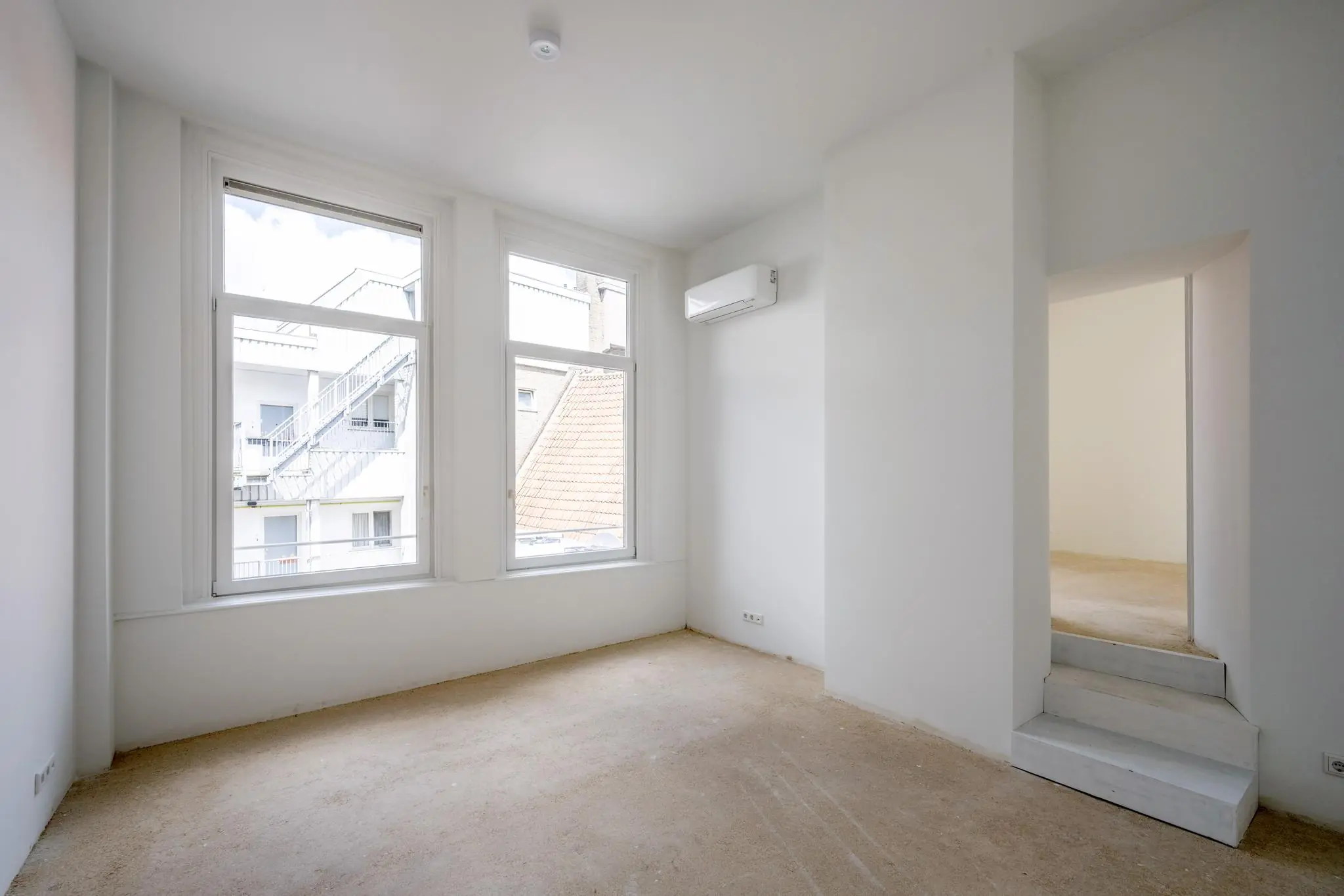 Lichte, lege kamer aan het Damrak met twee grote ramen, witte muren, airconditioning en doorgang naar aangrenzende ruimte.