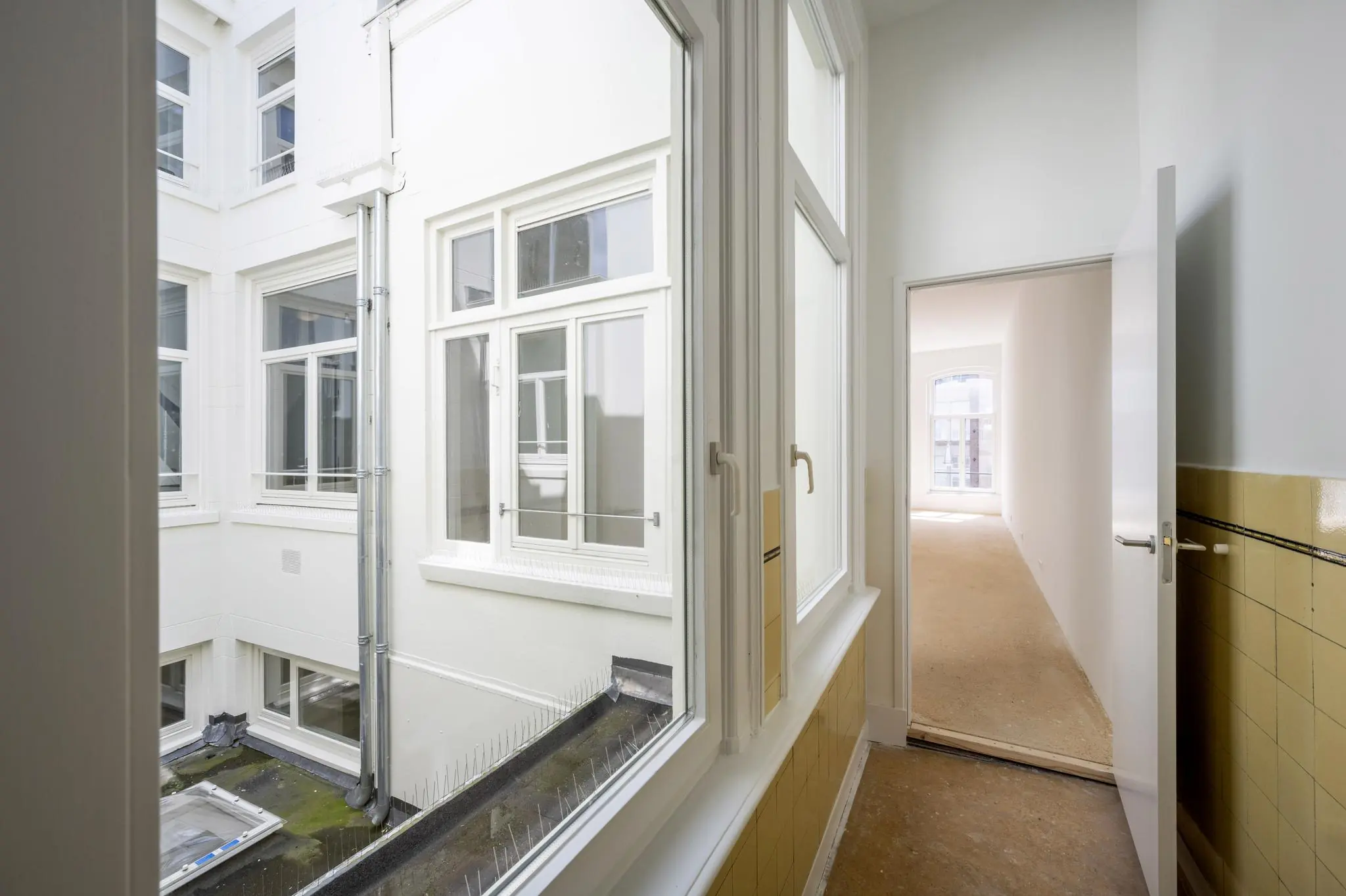 Binnenaanzicht van een licht trappenhuis op het Damrak met uitzicht op een binnenplaats en een aangrenzende kamer.