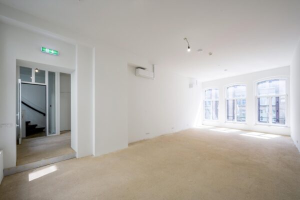 Licht en leeg interieur van een ruimte aan het Damrak met grote ramen en een betonnen vloer.