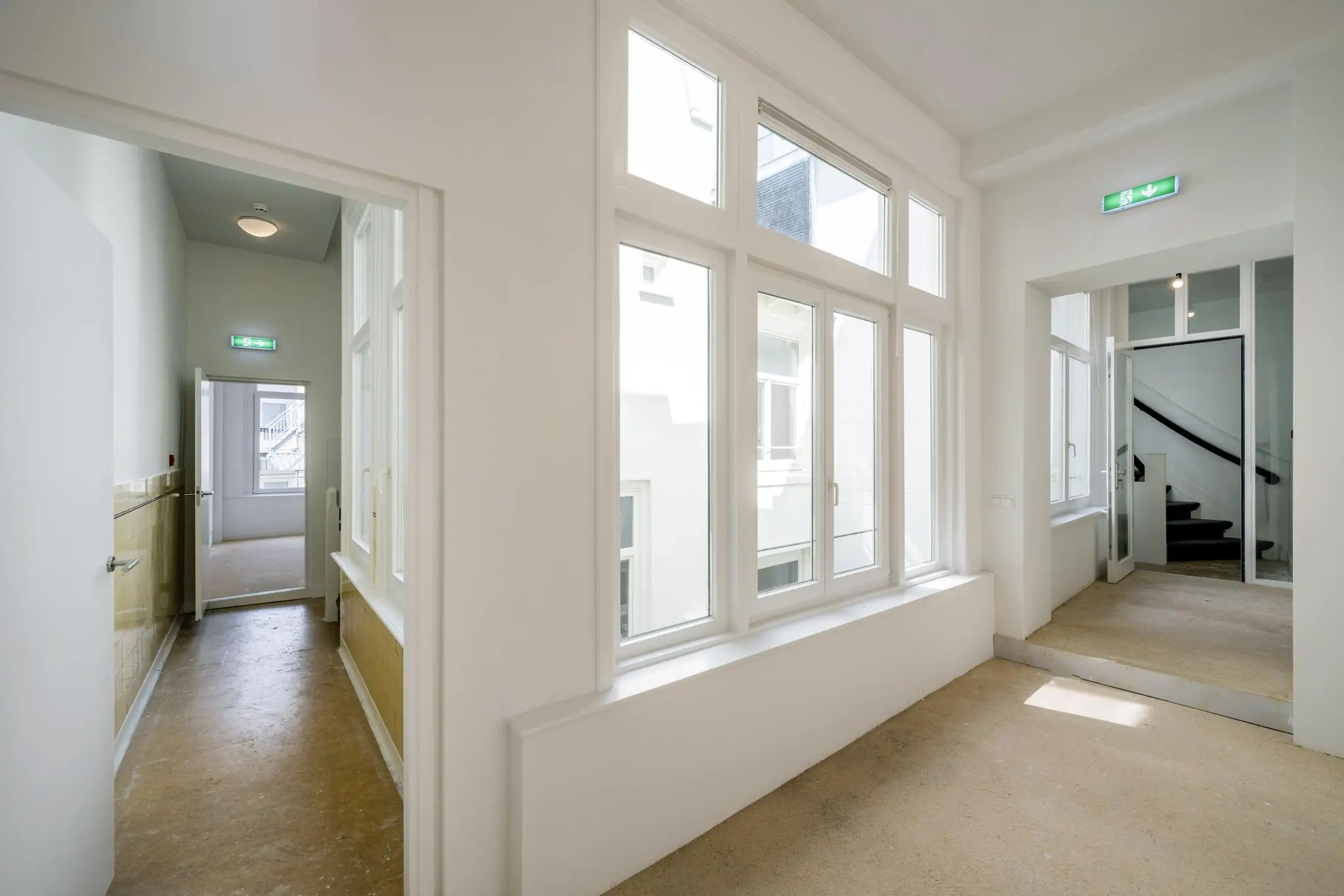 Licht en ruim binnenhal met grote ramen en zicht op een trappenhuis in een pand aan het Damrak.