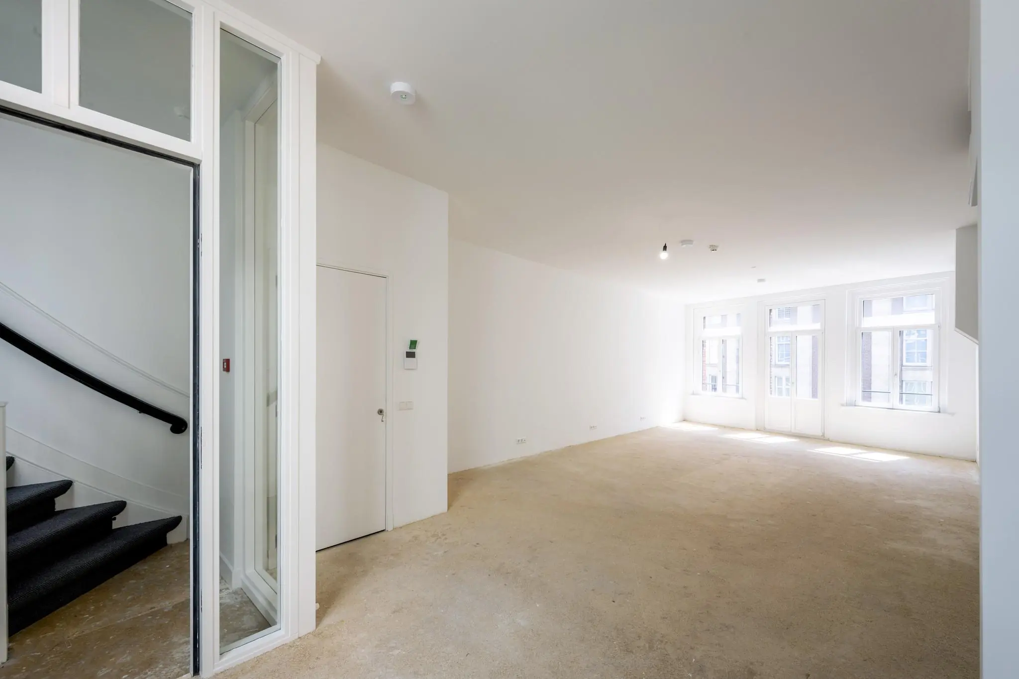 Lichte, lege woonruimte aan het Damrak met grote ramen en open trap naar boven.