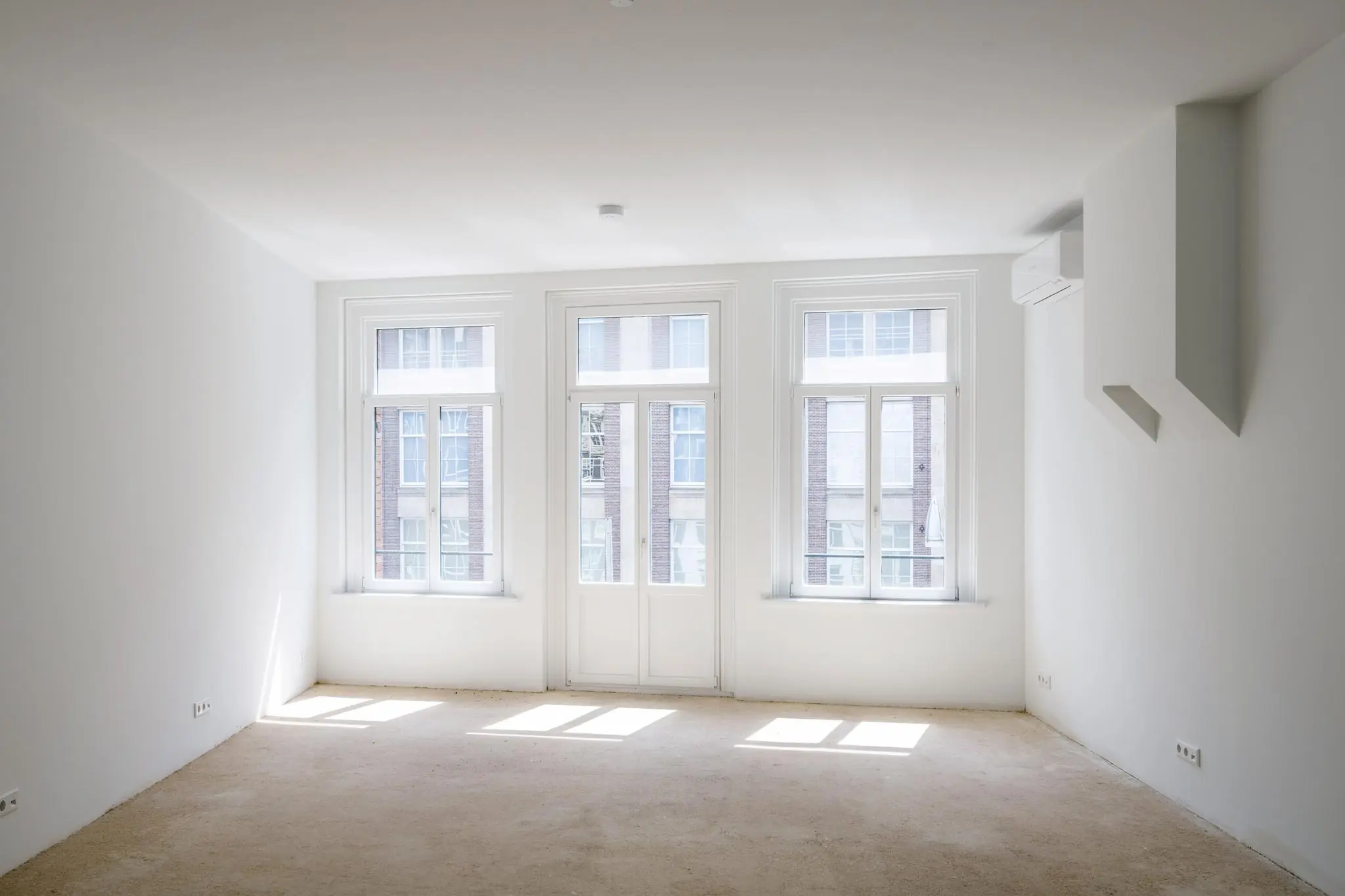 Licht en leeg appartement aan het Damrak met drie grote ramen en een deur naar een Frans balkon.