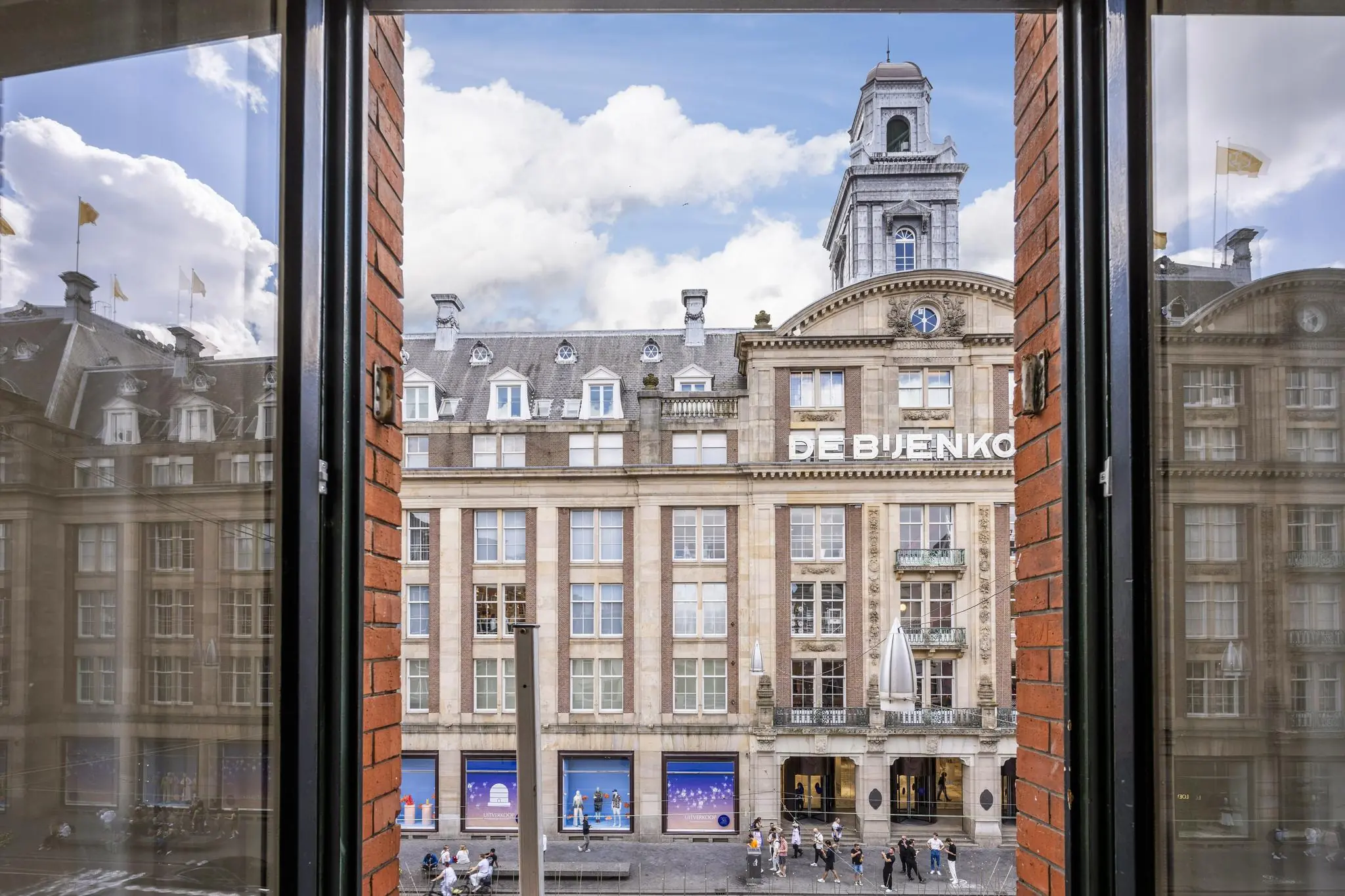 Uitzicht vanuit een open raam op het historische warenhuis De Bijenkorf aan het Damrak in Amsterdam.