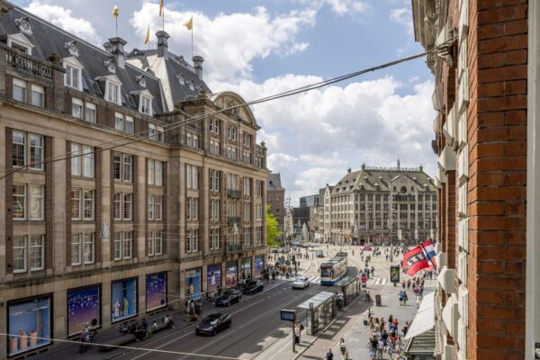 Druk stadsbeeld van het Damrak in Amsterdam met historische gebouwen, trams en voetgangers.