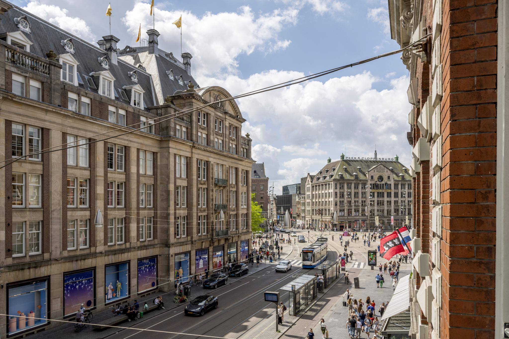 Druk stadsbeeld van het Damrak in Amsterdam met historische gebouwen, trams en voetgangers.