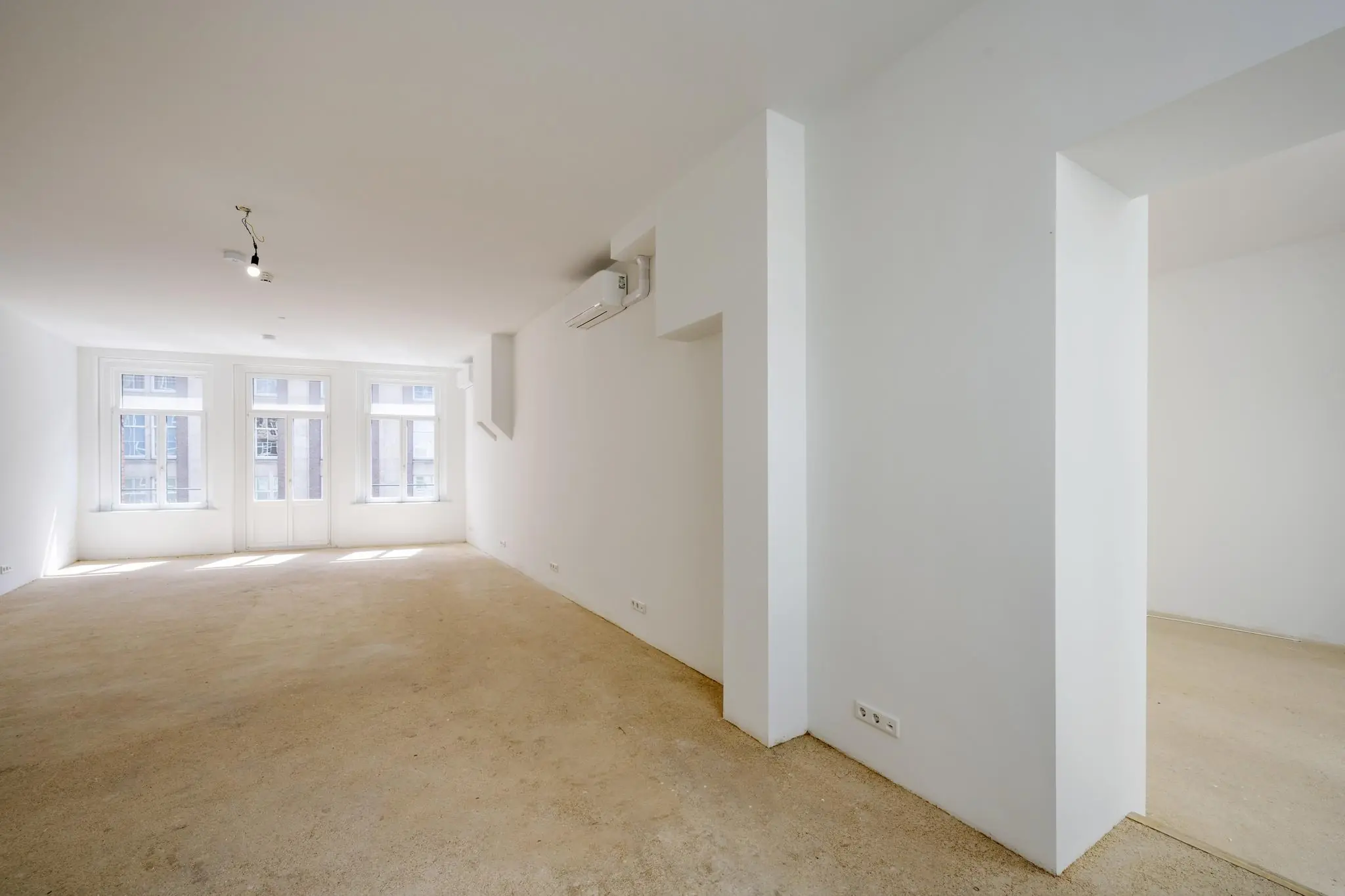 Licht en ruim leegstaand appartement aan het Damrak met grote ramen en witte muren.