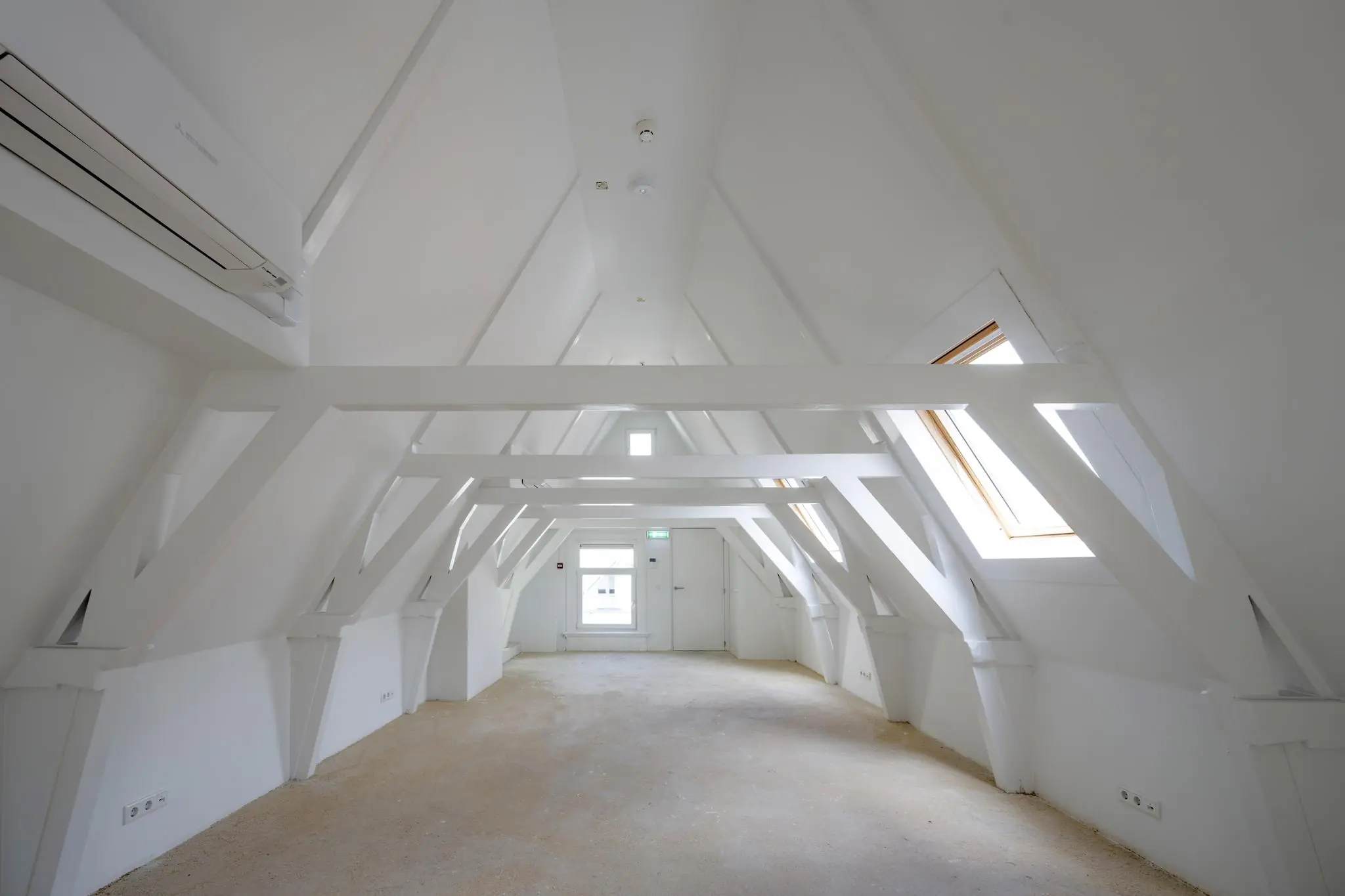 Zolderruimte aan het Damrak met witte houten balken, schuine dakramen en een onafgewerkte vloer.