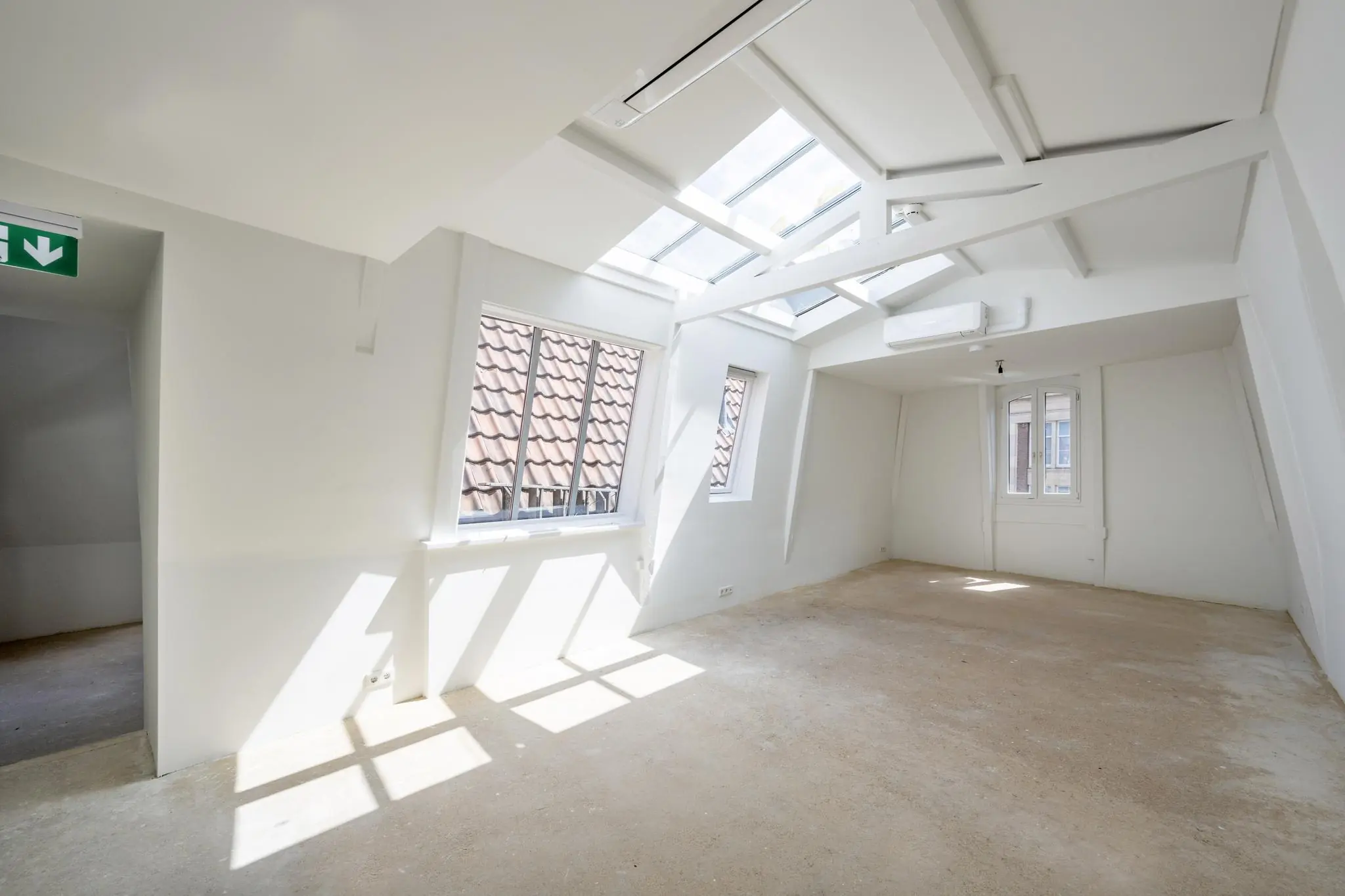 Licht zolderappartement aan het Damrak met schuine wanden, dakramen en zicht op rode dakpannen.