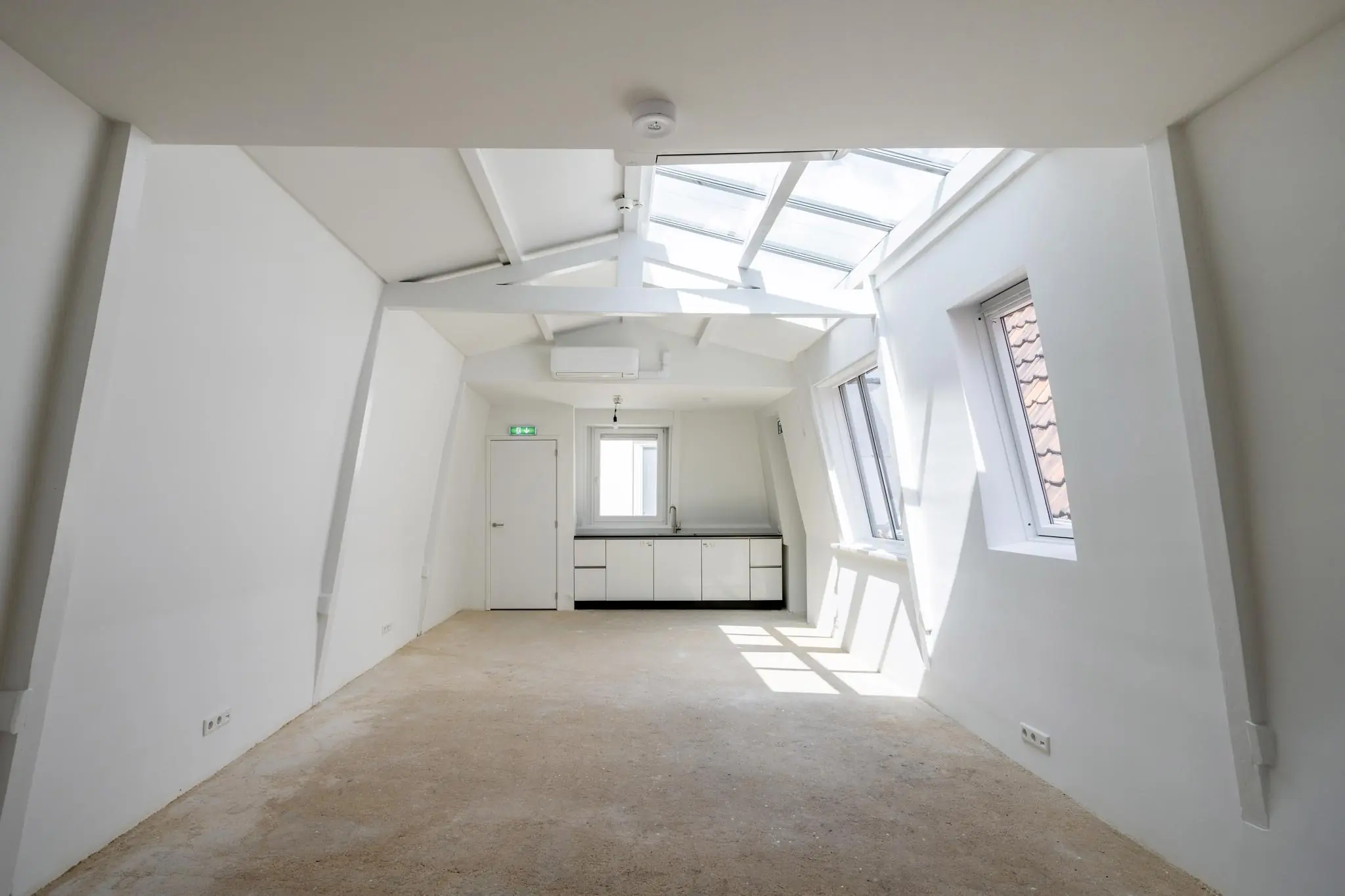 Lichte, lege zolderruimte aan het Damrak met wit interieur, schuine wanden en dakramen.