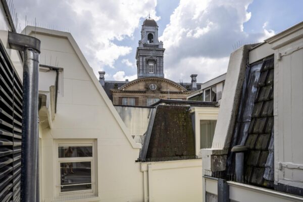 Uitzicht op het historische gebouw aan het Damrak in Amsterdam tussen de daken van omliggende panden.