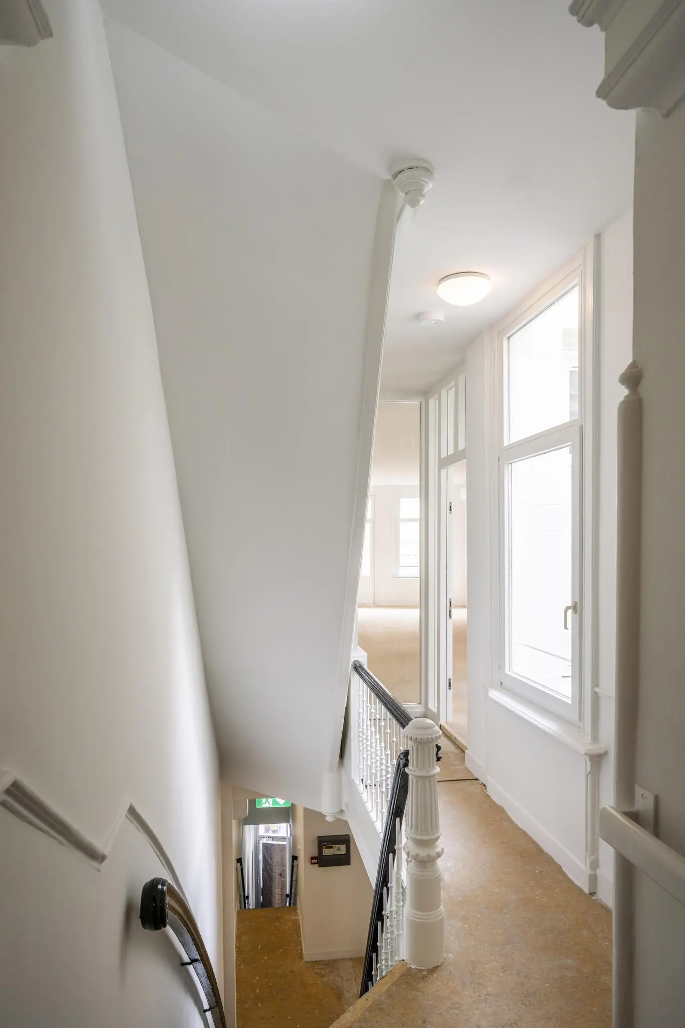 Trappenhuis met witgeschilderde muren, houten leuning en grote ramen in een pand aan het Damrak.