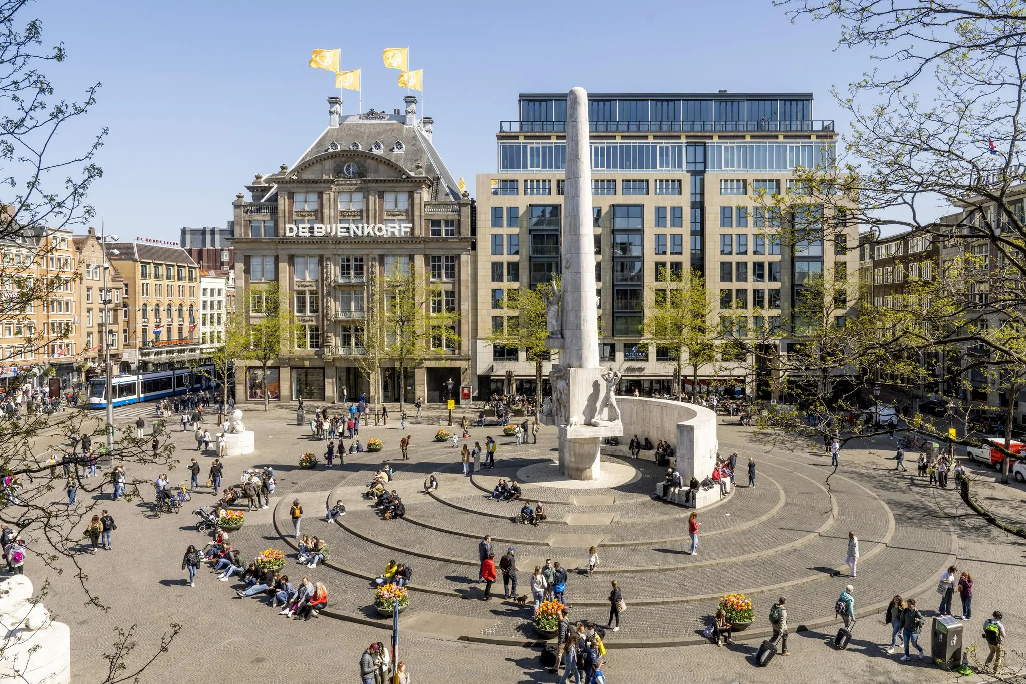 Druk bezochte Dam in Amsterdam met het Nationaal Monument en warenhuis De Bijenkorf op de achtergrond.