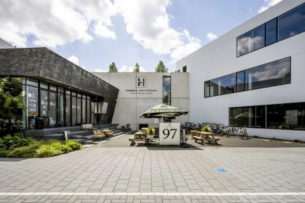 Vooraanzicht van het moderne kantoorpand Handel Amsterdam aan de Fred. Roeskestraat met terras en fietsenstalling.