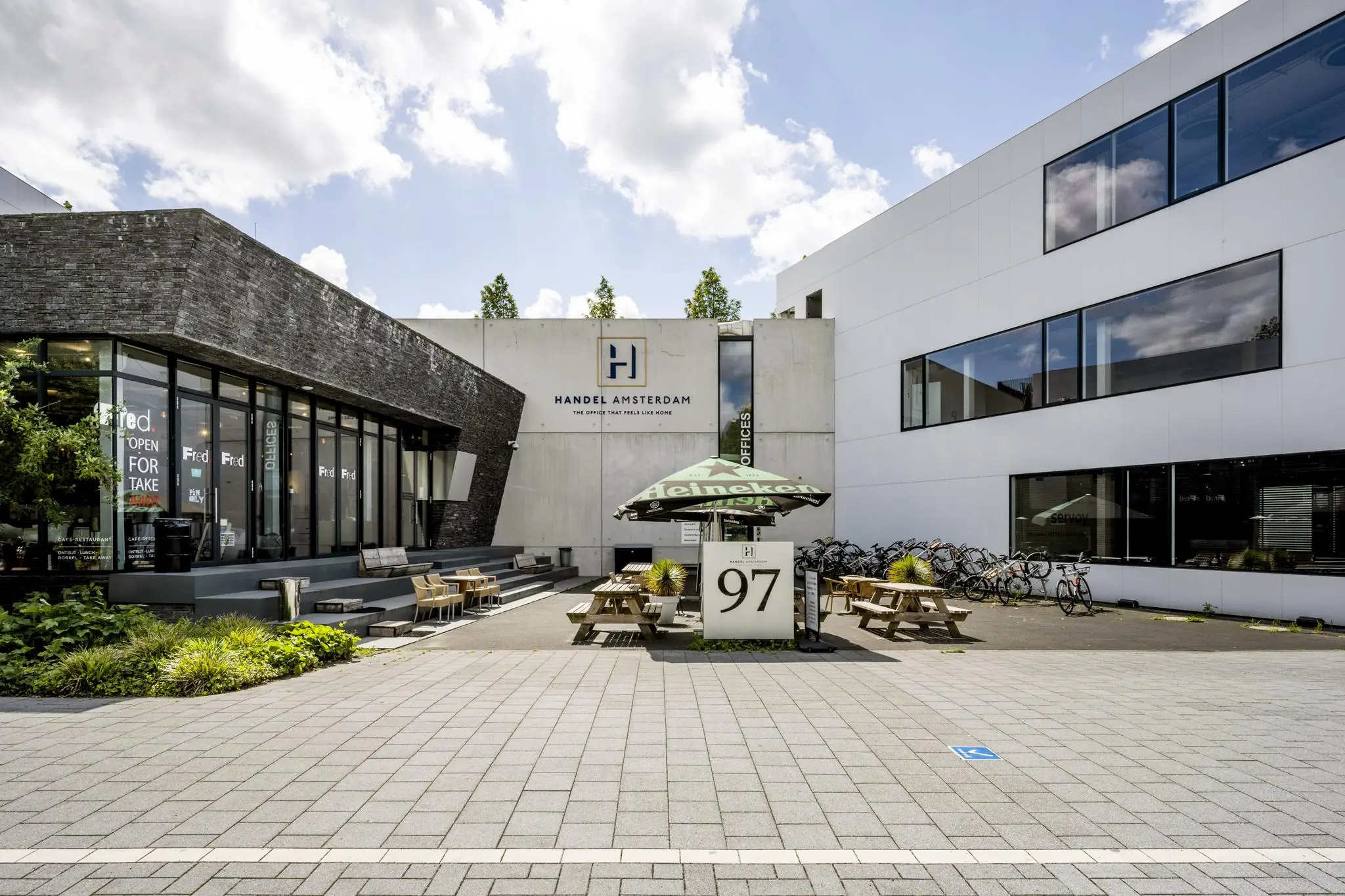 Vooraanzicht van het moderne kantoorpand Handel Amsterdam aan de Fred. Roeskestraat met terras en fietsenstalling.