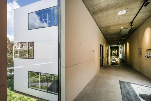 Doorkijk vanuit een betonnen gang naar de moderne witte gevel van een gebouw aan de Fred. Roeskestraat.