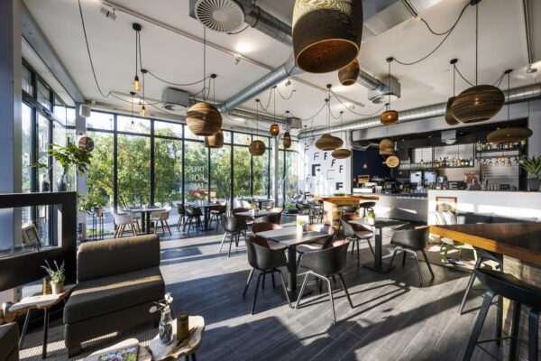 Modern en licht café aan de Fred. Roeskestraat met grote ramen, houten accenten en een gezellige zithoek.