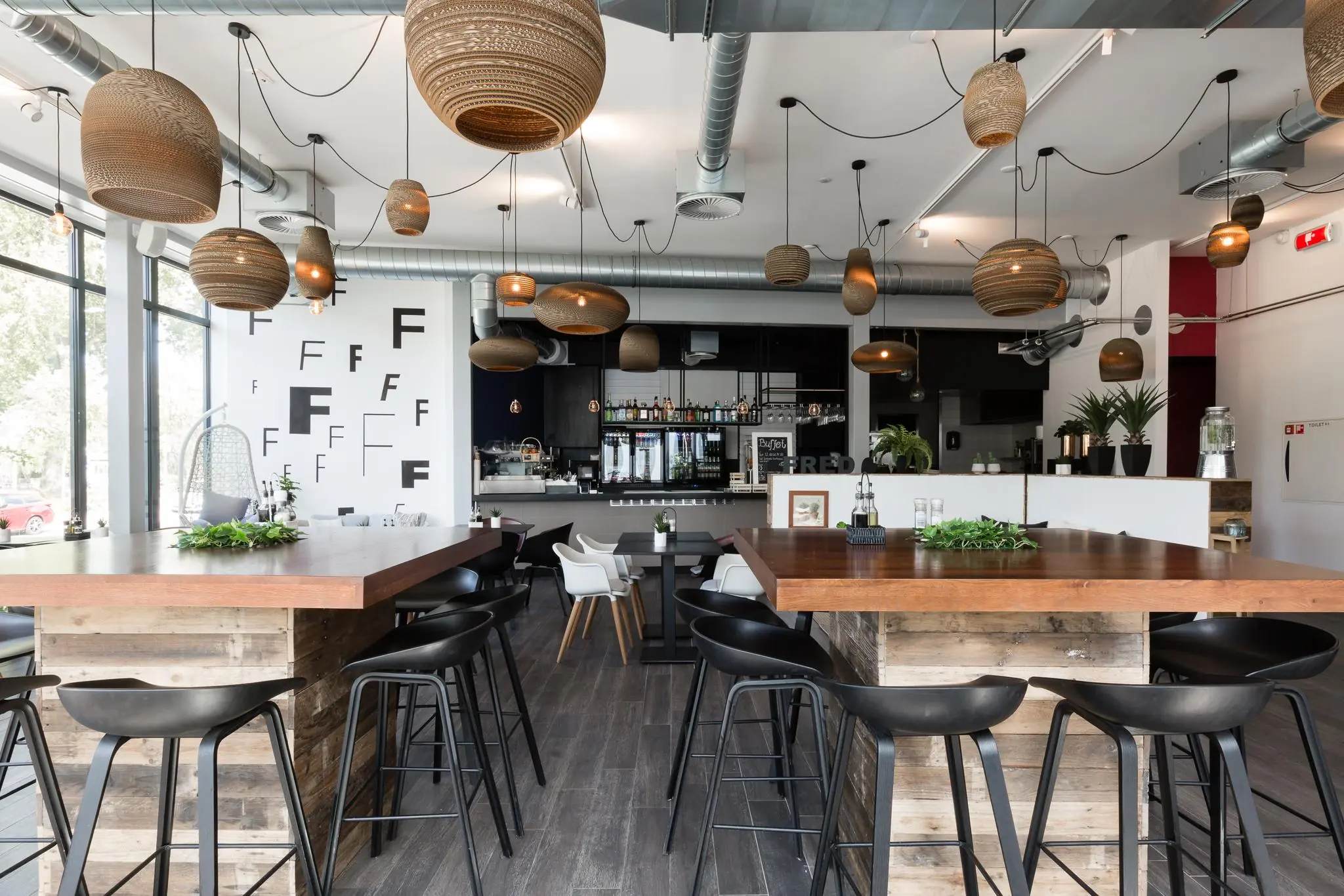 Modern interieur van een restaurant of café aan de Fred. Roeskestraat met houten tafels, zwarte barkrukken en hanglampen van gevlochten materiaal.