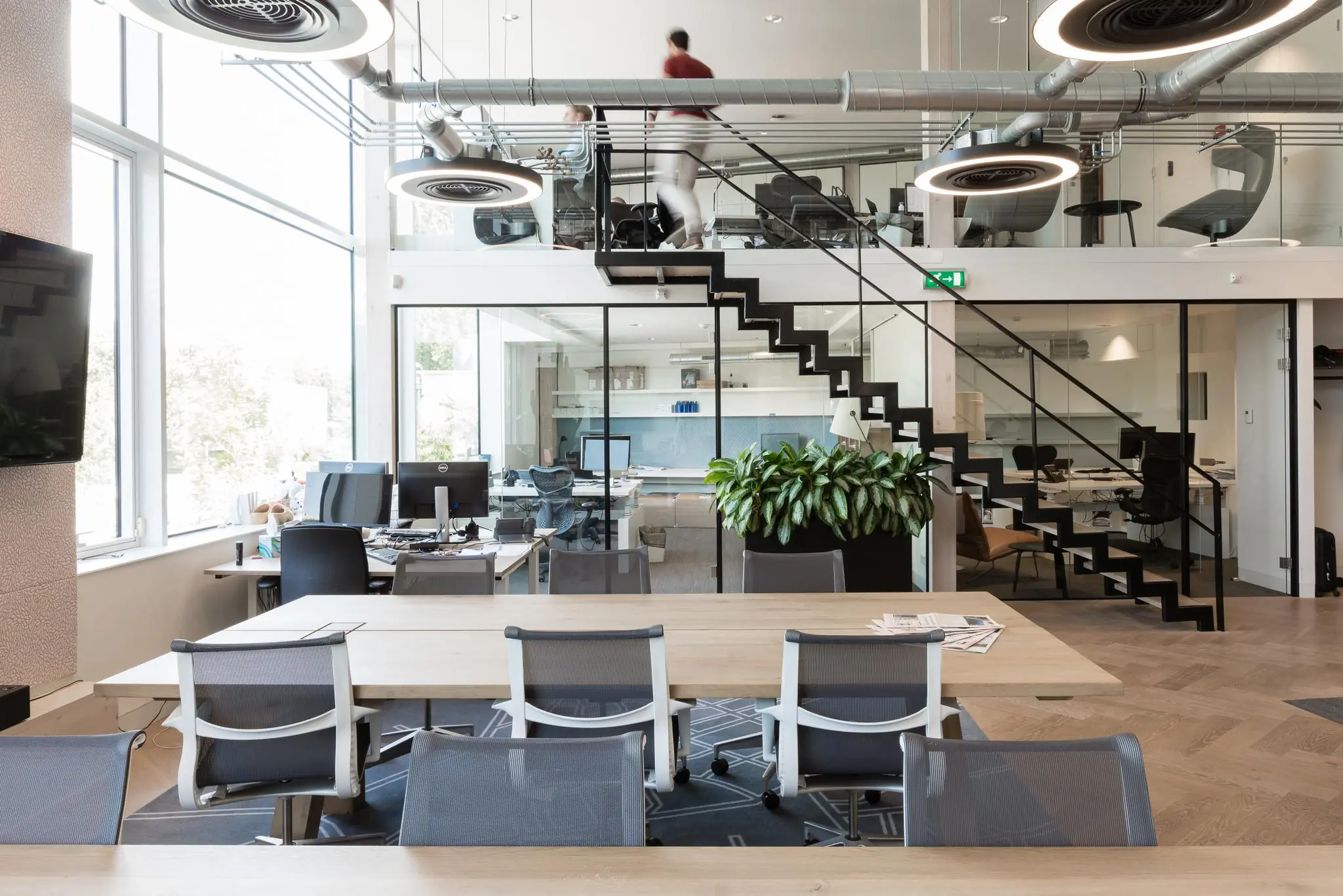 Modern kantoorinterieur aan de Fred. Roeskestraat met open werkplekken, glazen vergaderruimtes en een industriële trap naar de bovenverdieping.
