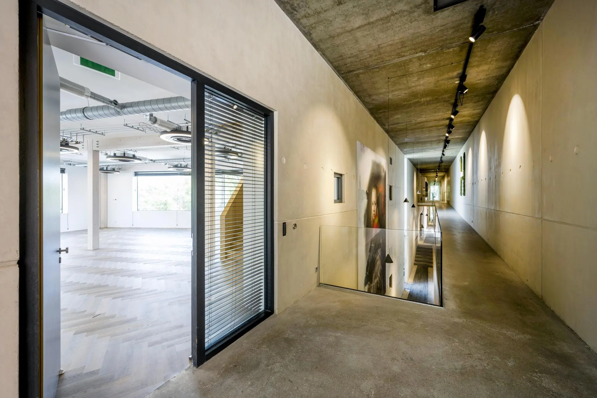 Moderne betonnen gang met zicht op een open kantoorruimte en trapgat in het Fred. Roeskestraat-gebouw.