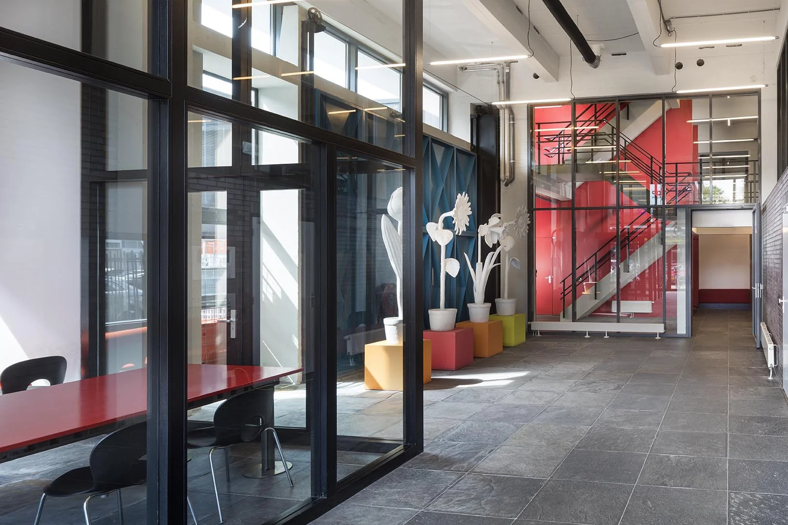 Moderne entree van een gebouw aan de Generaal Vetterstraat met felrode trapkast, grote raampartijen en kleurrijke decoratieve planten.