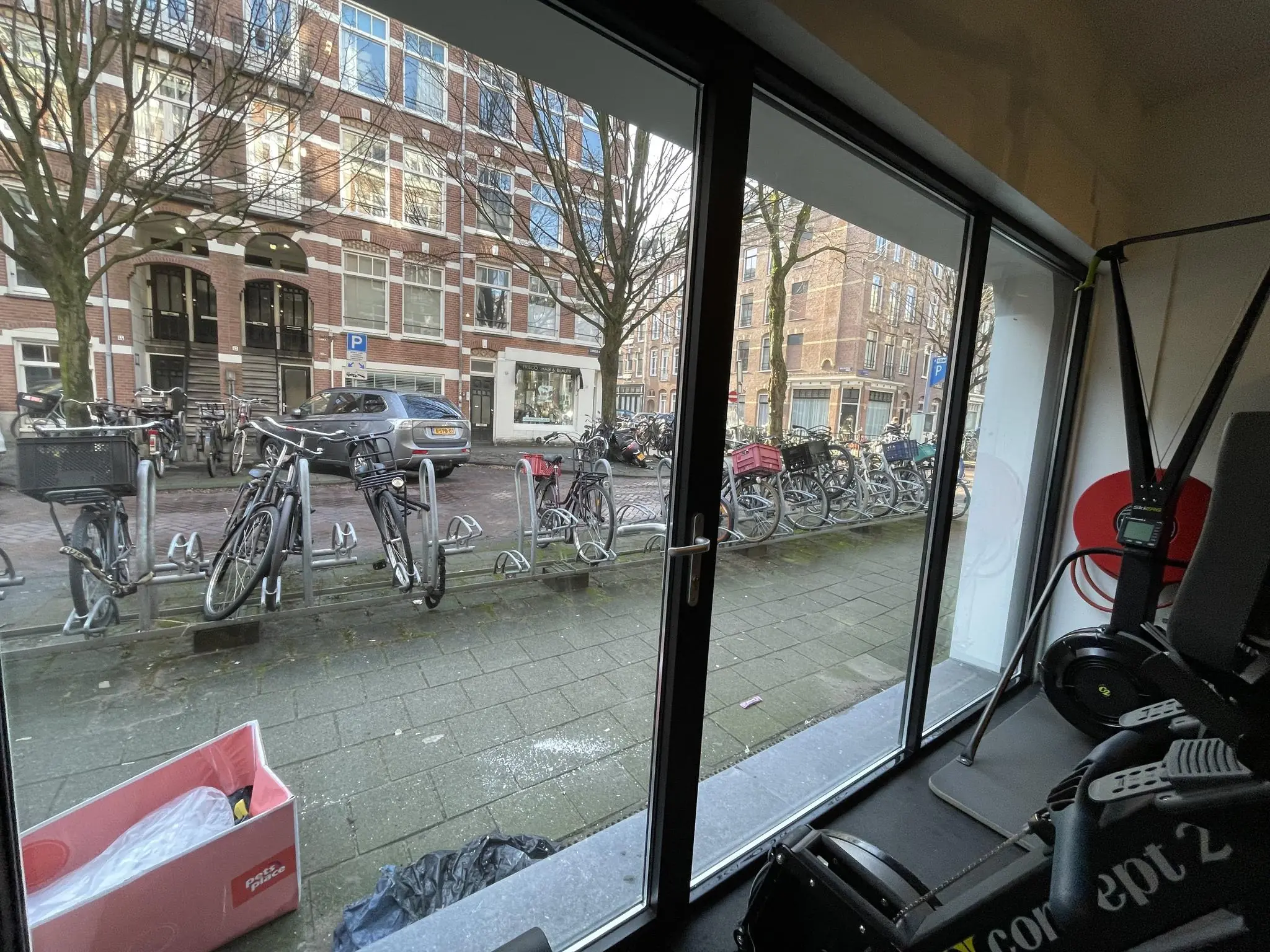 Uitzicht vanuit een sportschool aan de Pieter Baststraat op geparkeerde fietsen en een woonstraat in Amsterdam.