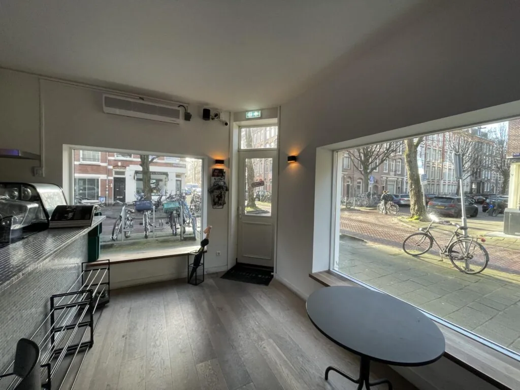 Interieur van een modern café aan de Pieter Baststraat met uitzicht op geparkeerde fietsen en een rustige straat door grote ramen.