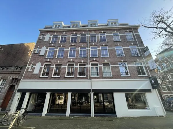 Voorgevel van een klassiek bakstenen pand aan de Pieter Baststraat met grote ramen en een commerciële ruimte op de begane grond.